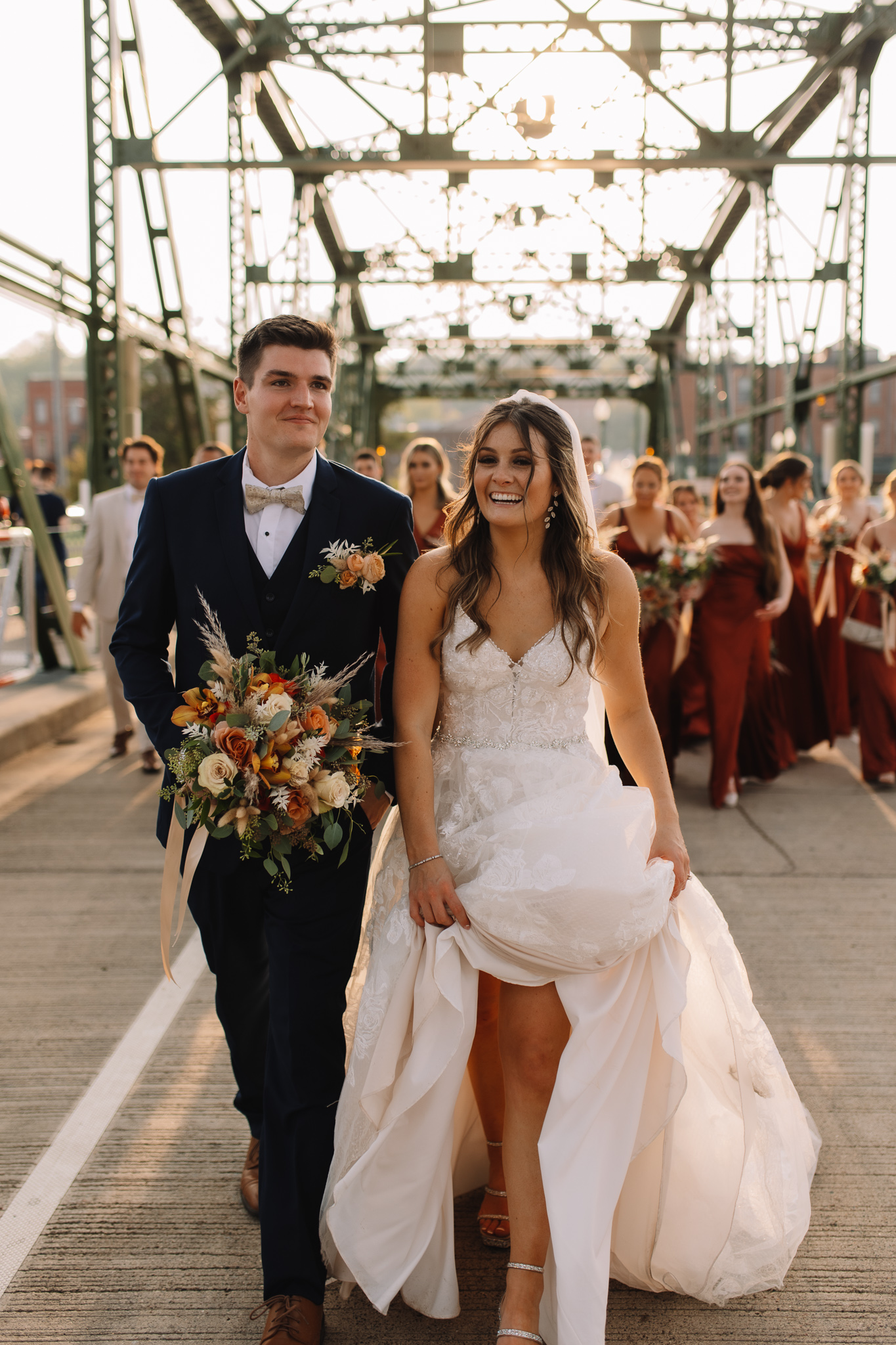 Bride and groom walking down the Stillwater bridge laughing during golden hour as their wedding party follows close behind them