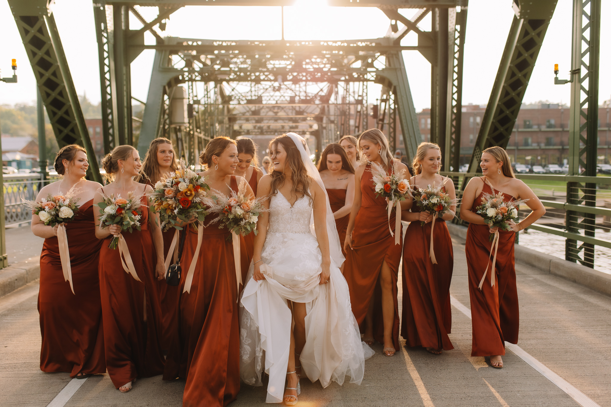 Professional wedding photography of a bride and her bridesmaids walking across the Stillwater bridge in Minnesota as the sun is setting