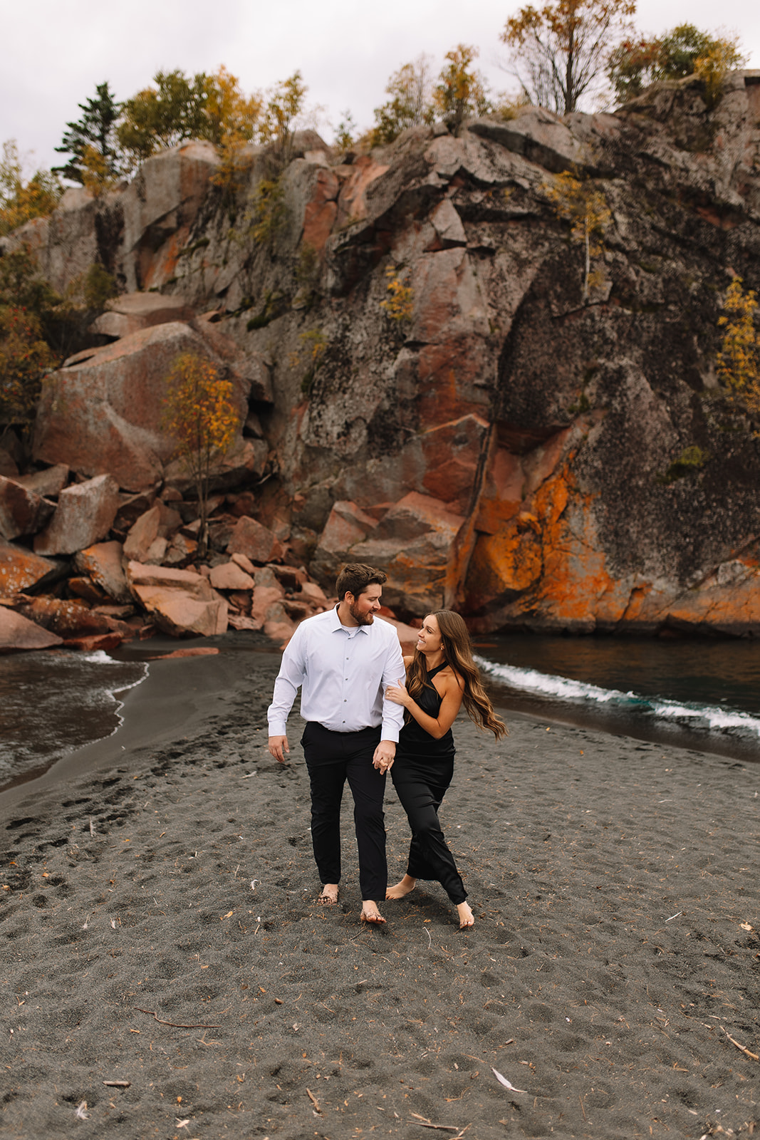 A wide shot photo of an engagement couple walking together on Black Sand Beach in Minnesota