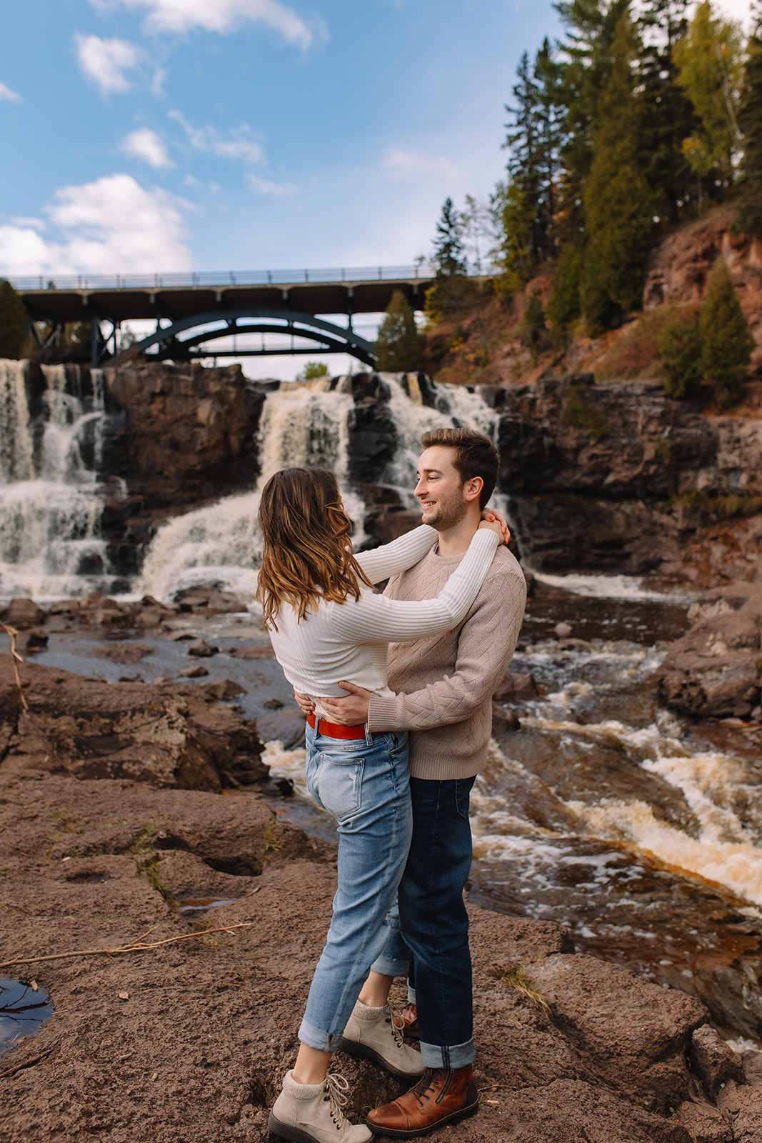 An engagement couple holding each other in an embrace in front of the Gooseberry Falls in Minnesota