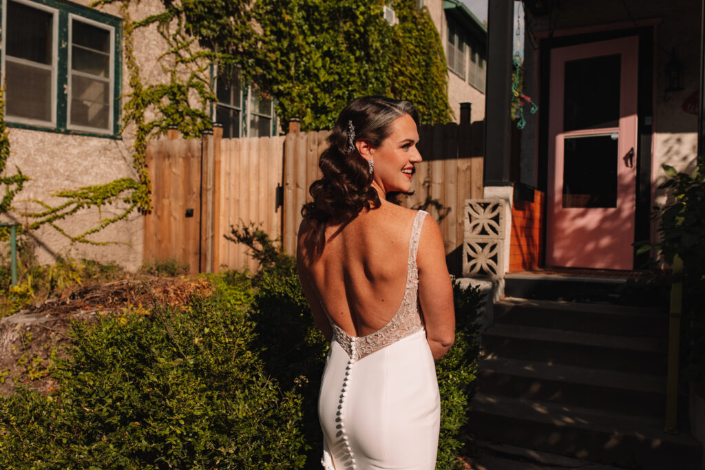 A bride with an open back wedding dress, standing in the sun with her back facing the camera.