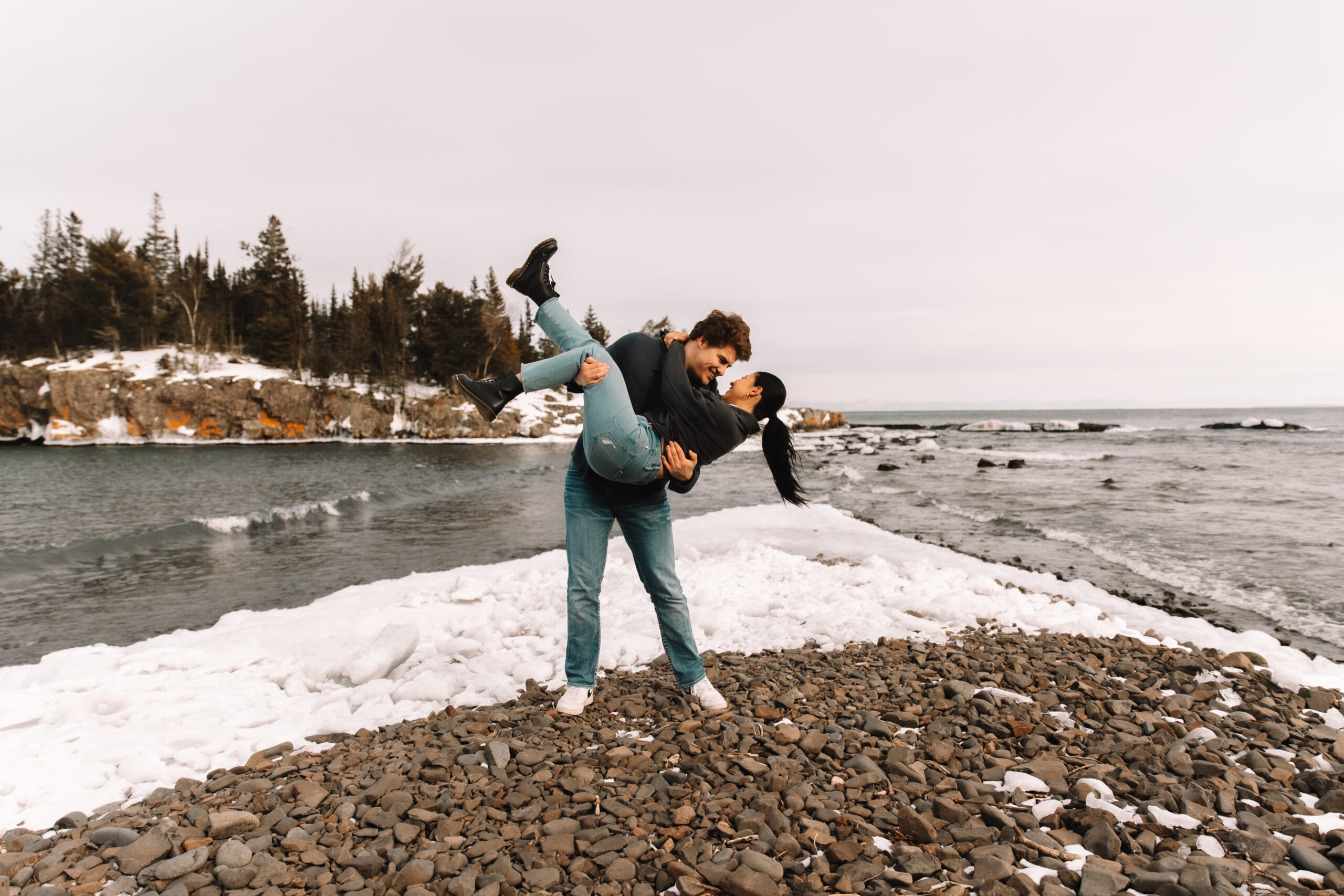 A man holding his girl in his arms, dipping her as they kiss with a beautiful snow covered back drop on the North Shore of Minnesota