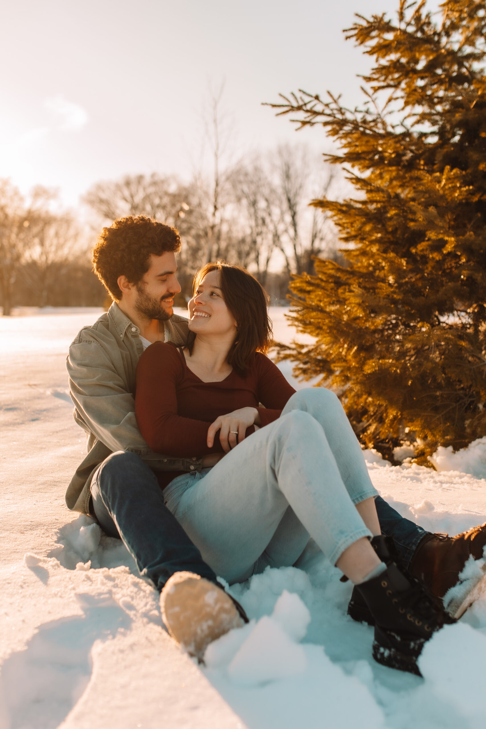 Newly engaged couple sitting in the snow smiling at one another