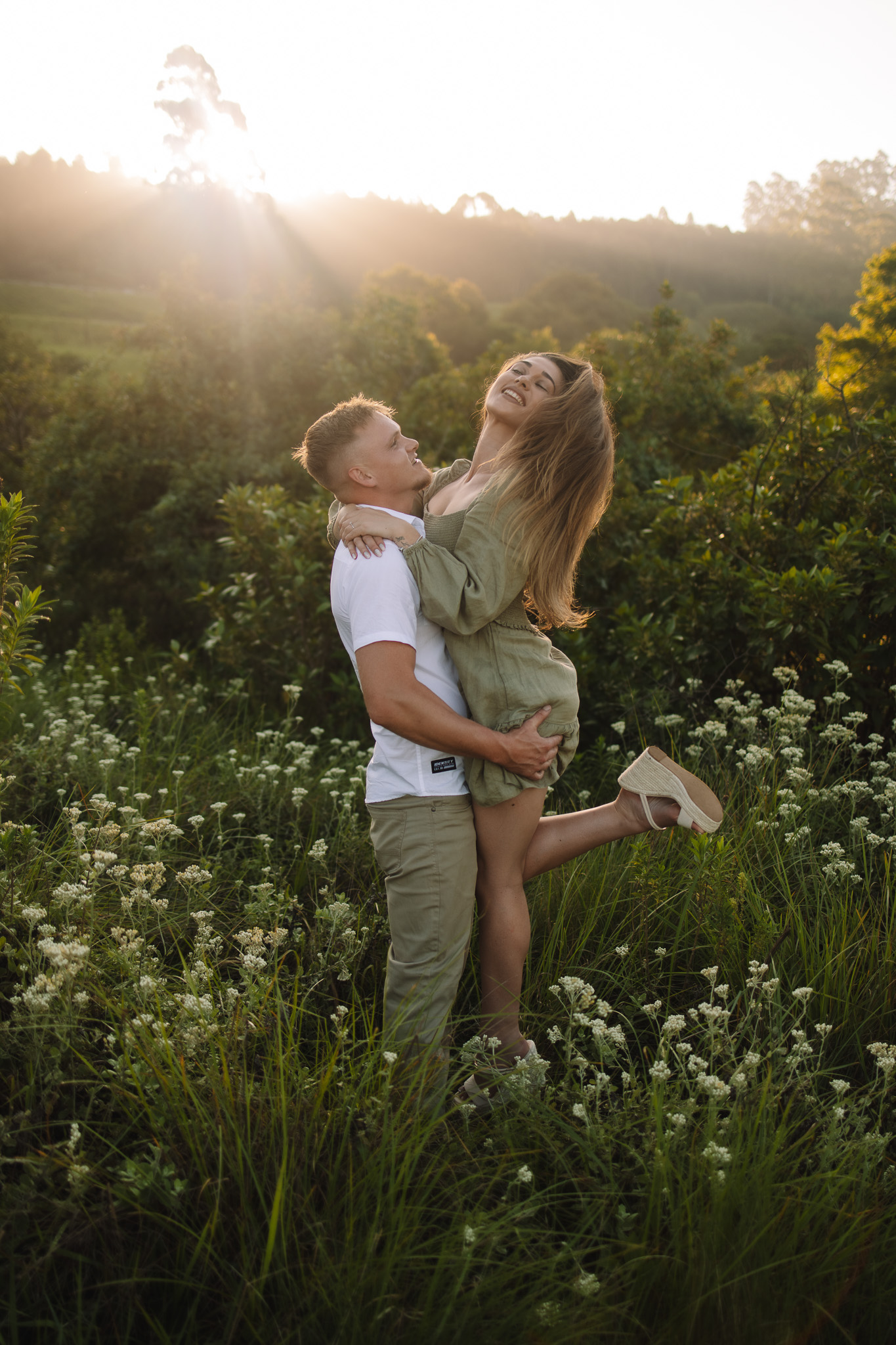 Engaged couple wearing cute engagement outfit in a flower field popping champagne, perfect inspiration to help you on what to wear for your engagement photos