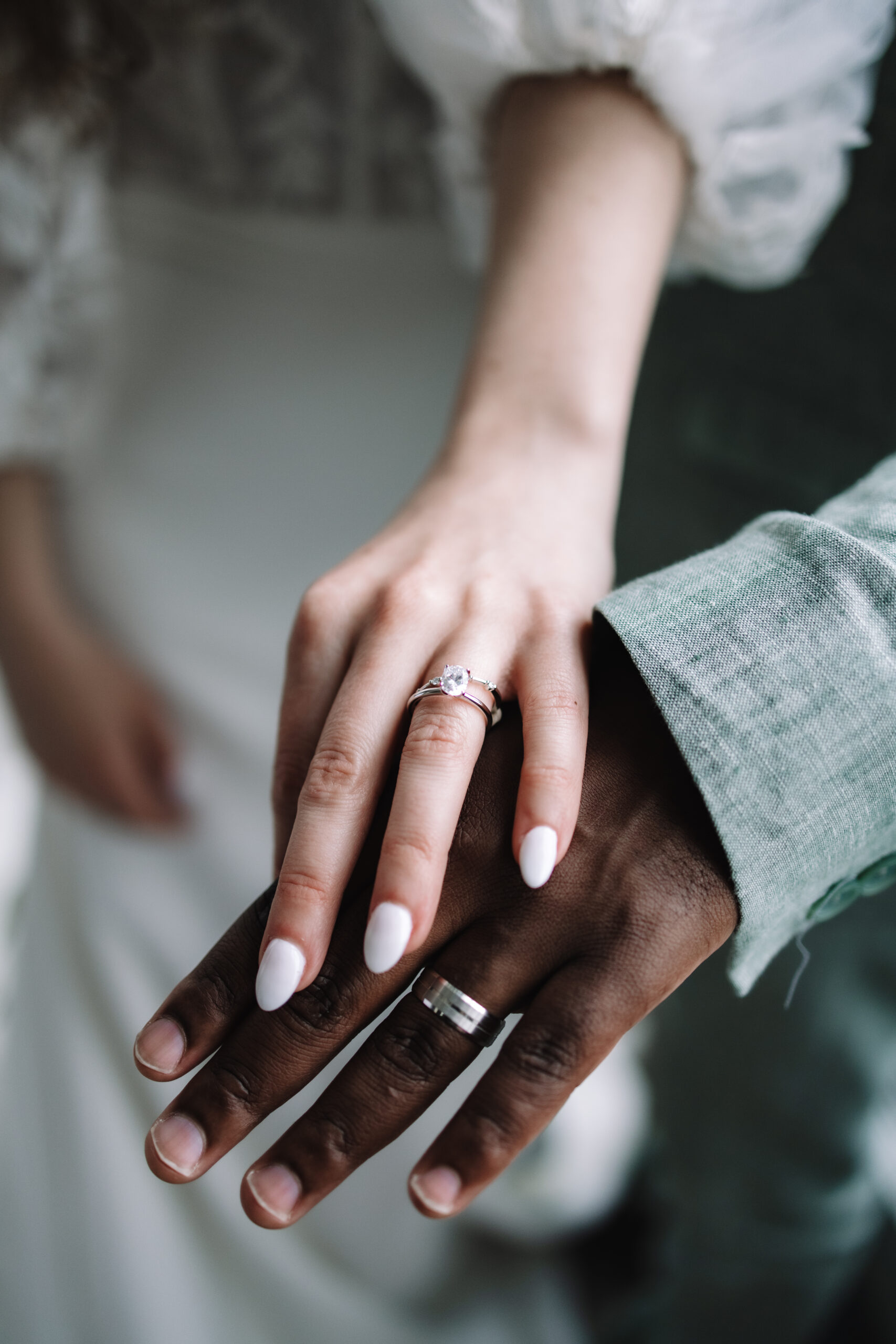 Close-up of a couple's hands, showcasing their wedding rings. The woman's hand has a diamond ring and manicured nails, while the man's hand wears a simple band.