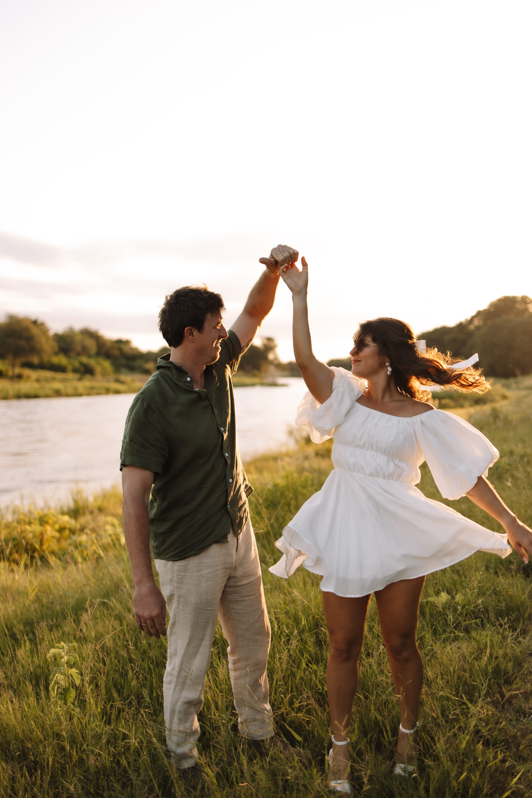 Newly engaged couple dancing in a field of grass near a lake in Minnesota