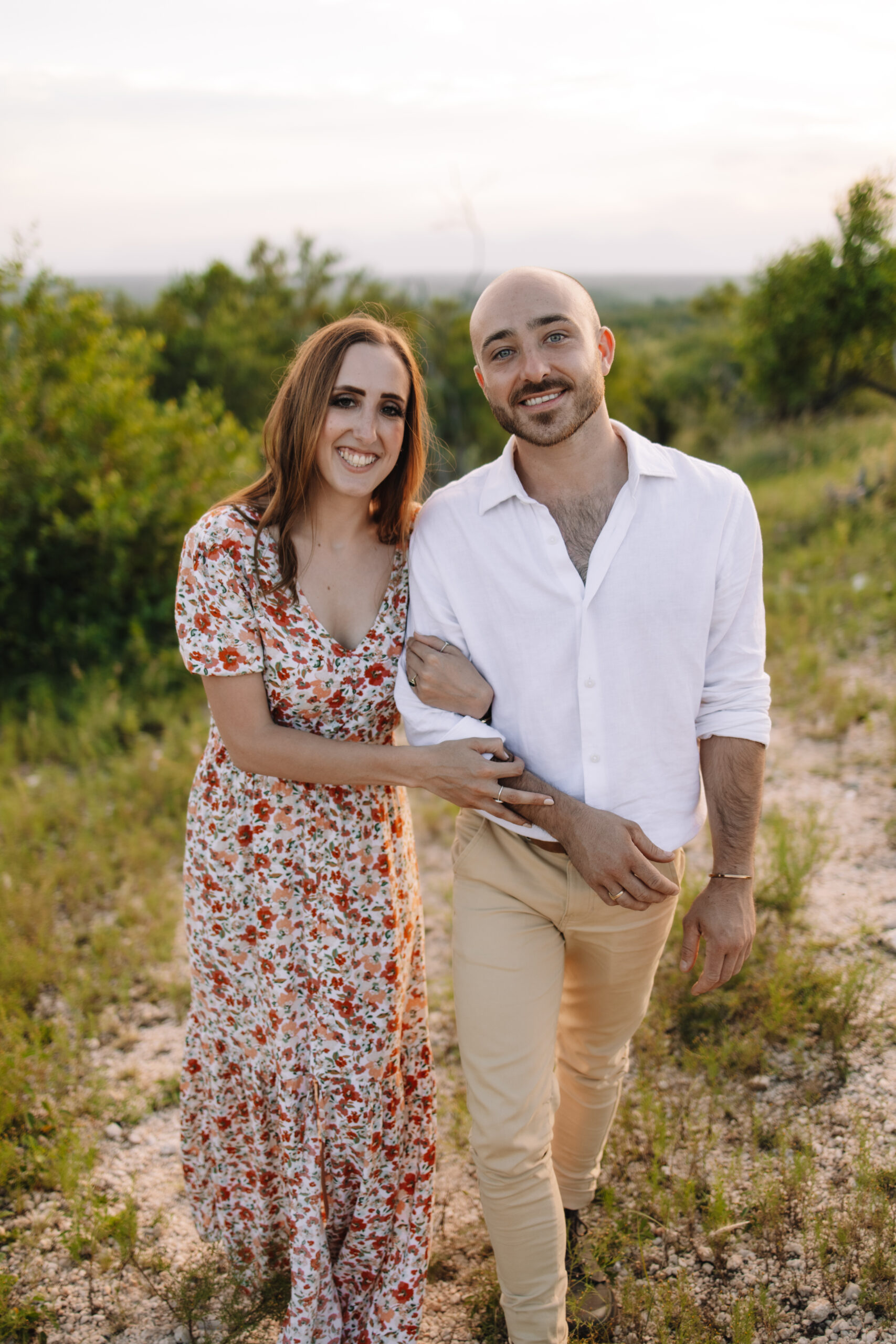 Newly engaged couple posing in a floral maxi dress and white button up and khaki pants for their engagement outfit