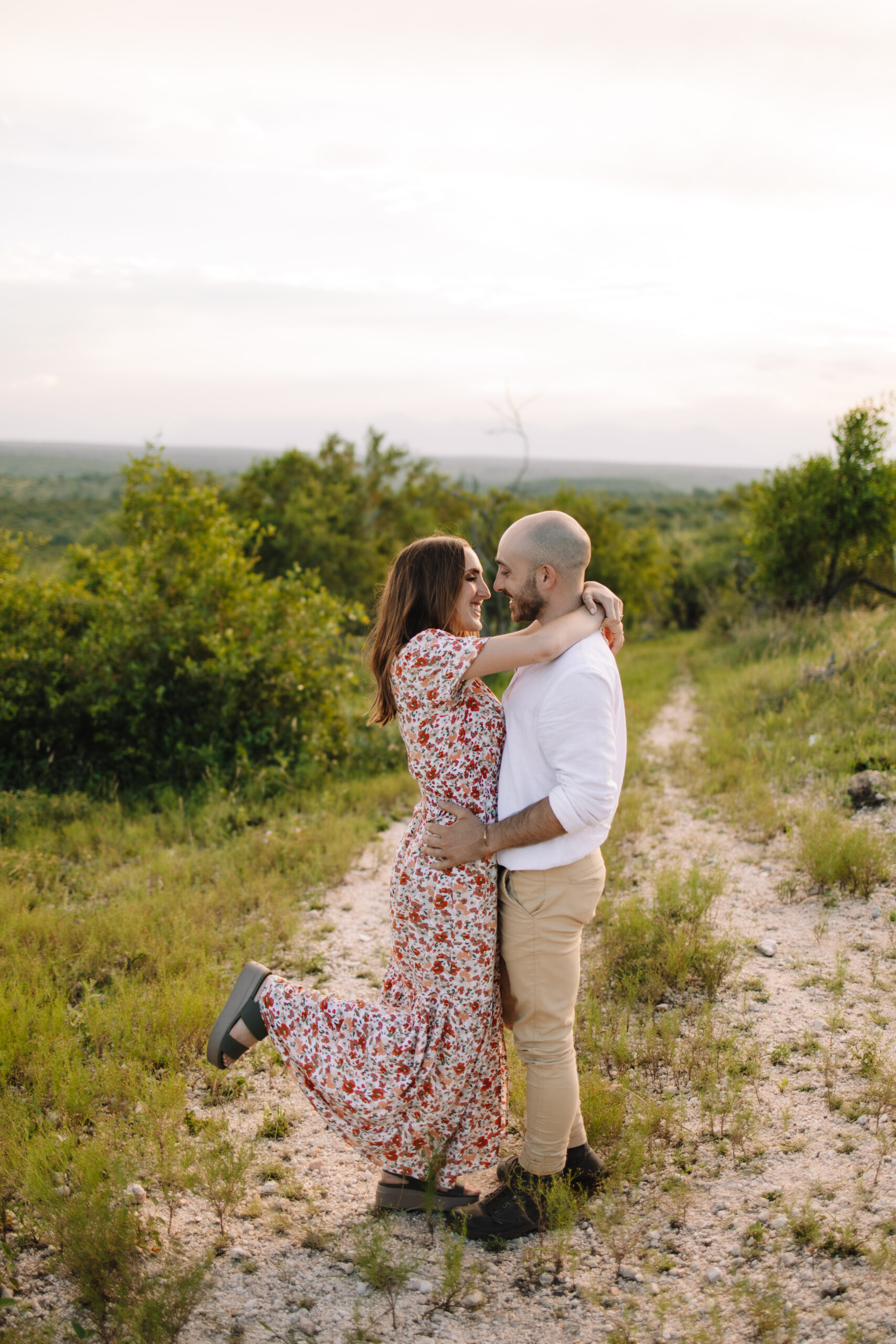 Newly engaged couple posing in a floral maxi dress and white button up and khaki pants for their engagement outfit