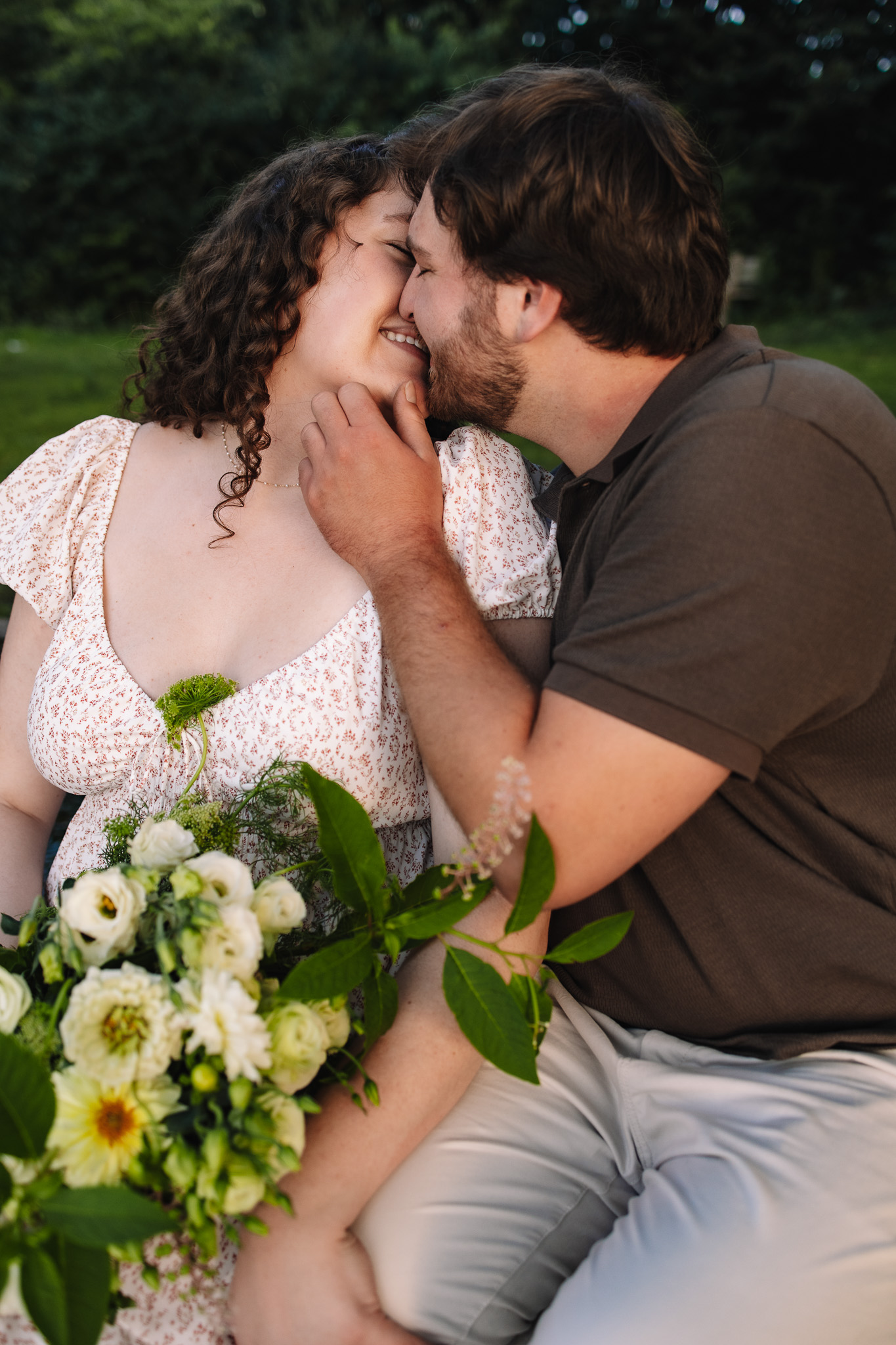 Newly engaged couple wearing co-ordinating engagement outfits with earthy tones, kissing each other tenderly