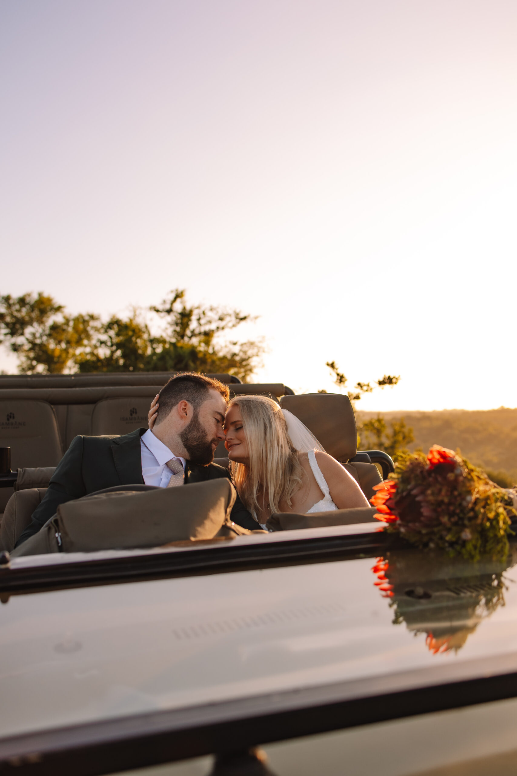 Destination wedding couple sitting together in the safari vehicle with a protea bouquet leaning on the dashboard