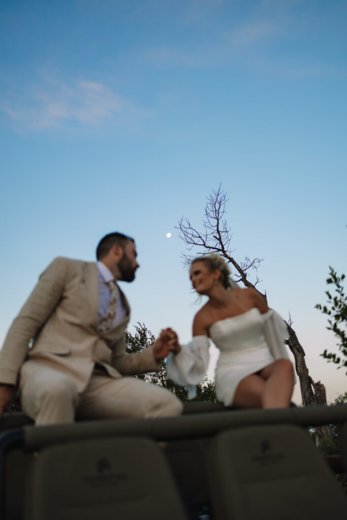 An elopement bride and groom sitting on a safari vehicle during blue hour with the moon behind them