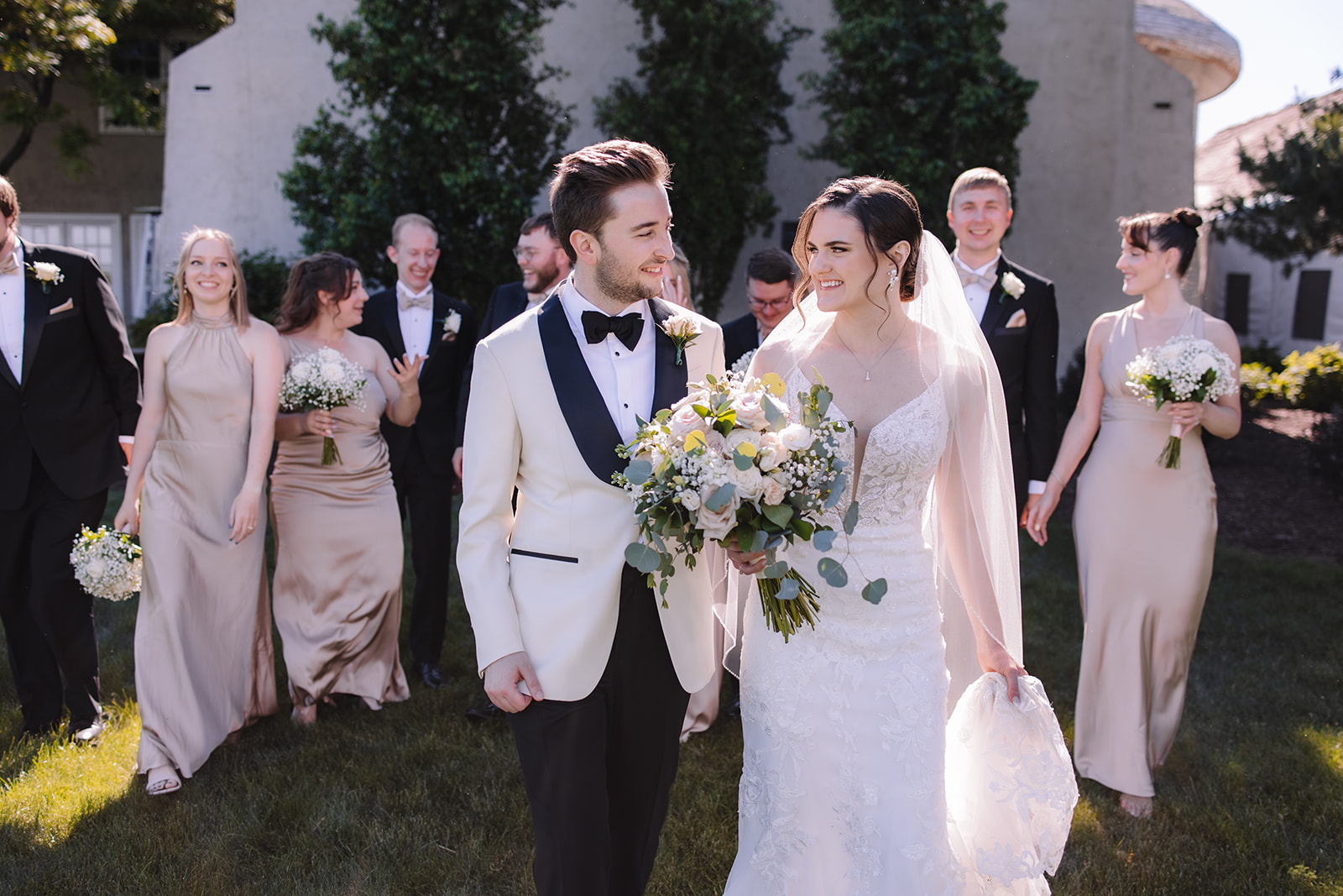 Bride and groom walking away from bridal party smiling at one another 