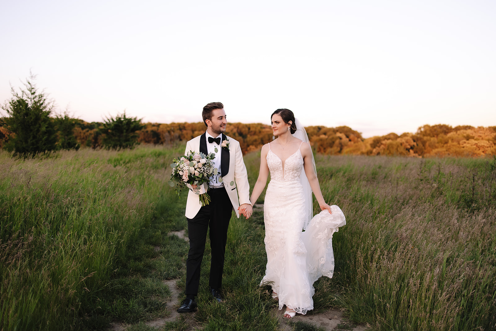 Bride and groom walking in a field of grass during sunset at Edward Anne Estate