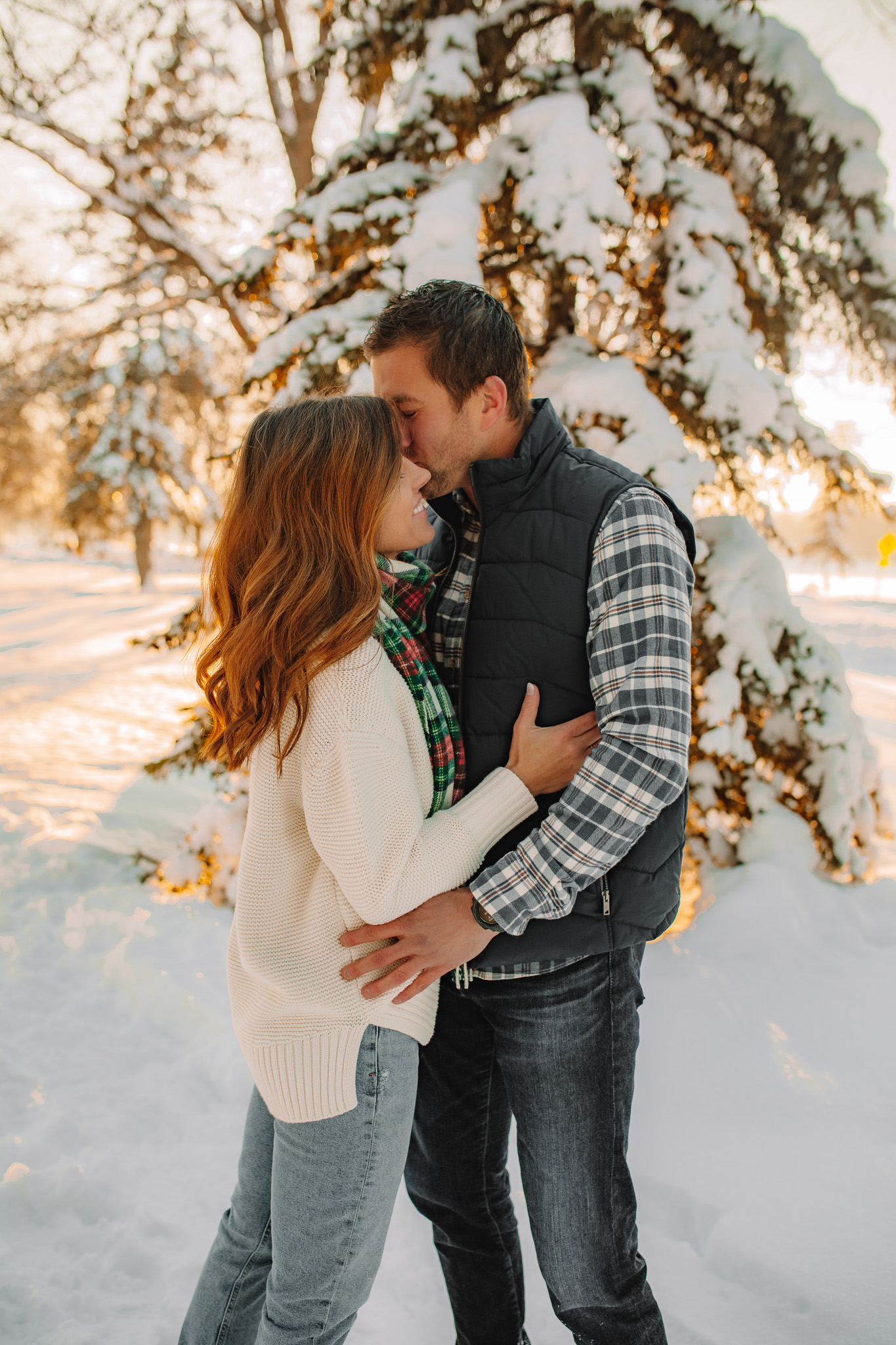 Newly engaged couple standing facing each other in the snow smiling at one another