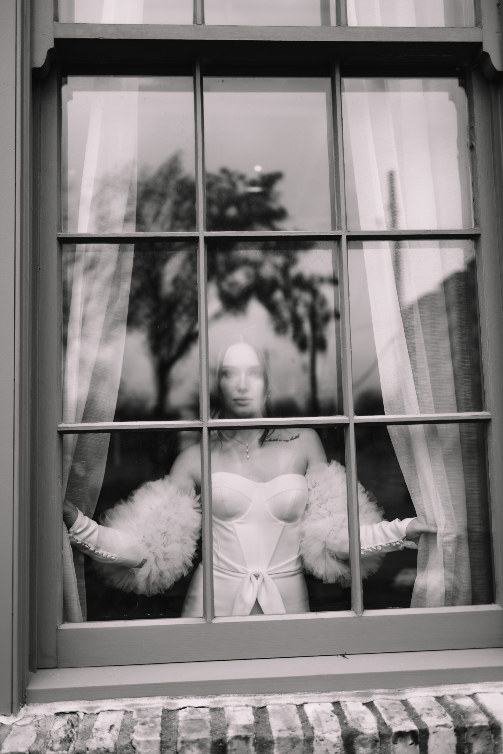 A person in a white outfit stands behind a window, holding the curtains open. The image is in black and white at the machine shop in Minneapolis