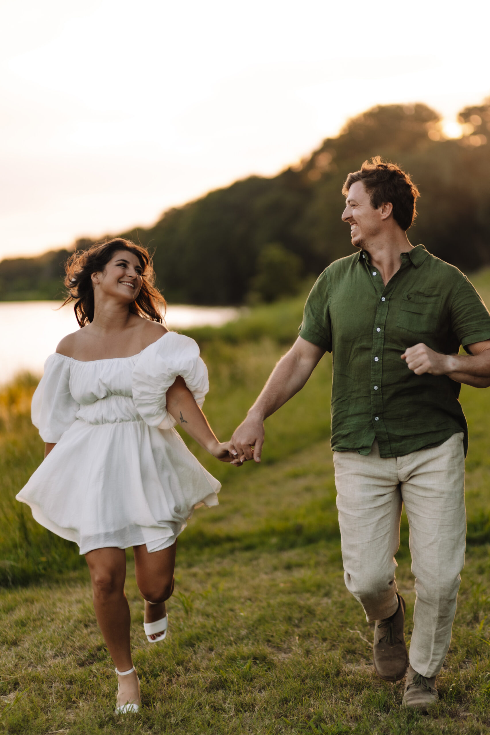 Newly engaged couple running holding hands smiling in a field of grass