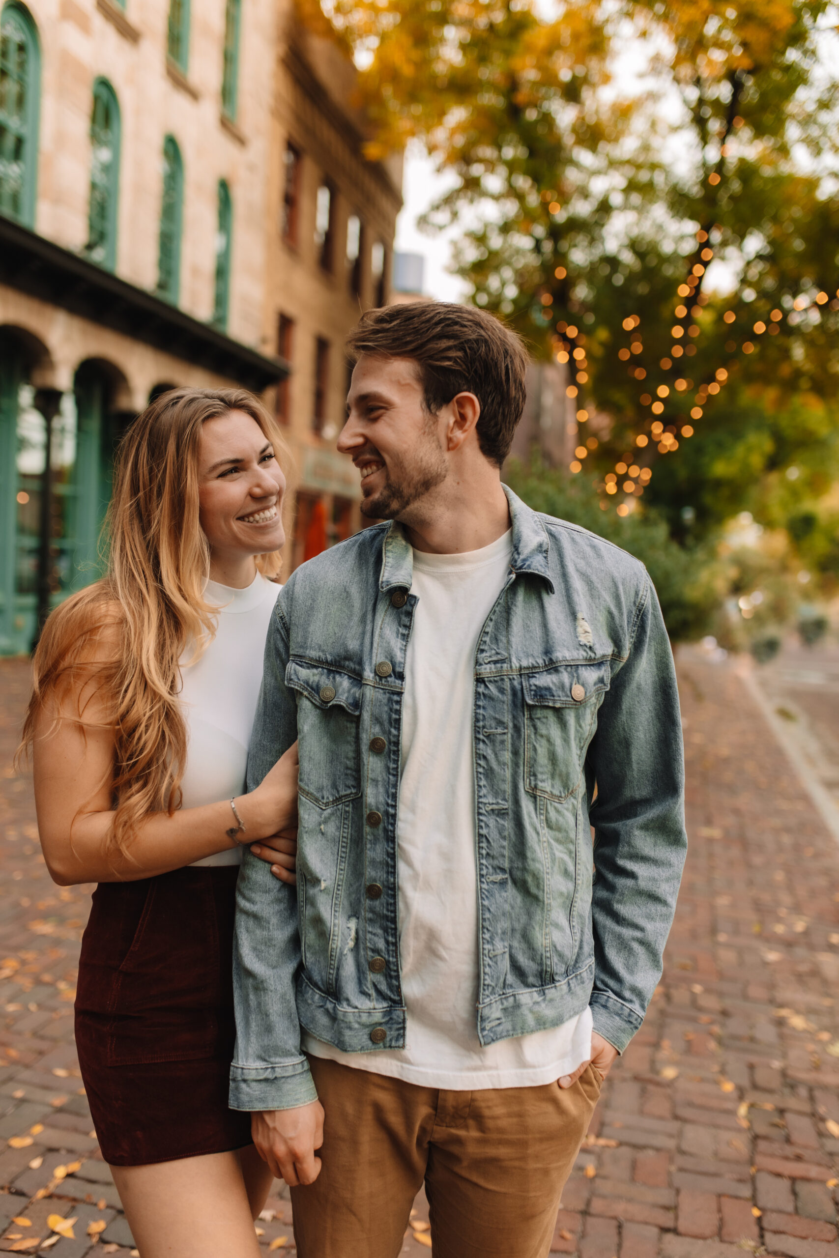 Newly engaged couple smiling at one another on cobblestone streets in Minnesota