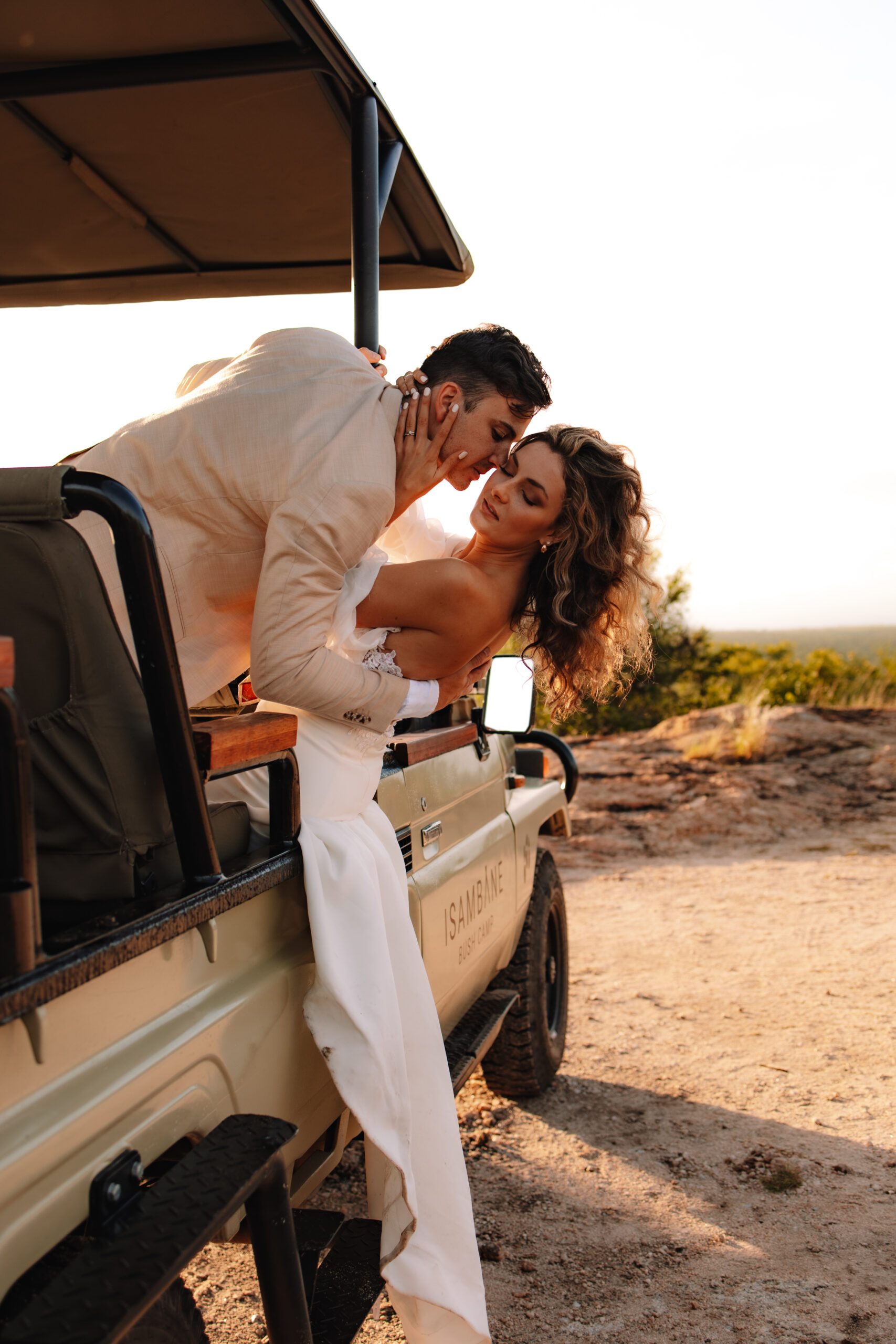 A bride and groom leaning out of the safari vehicle in South Africa with the Sun shining behind them