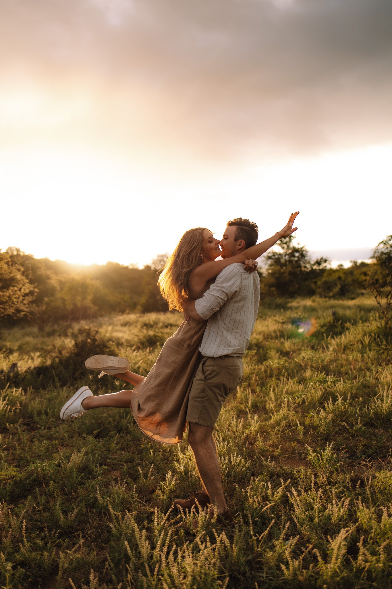 Guy picking up and spinning his fiancé around in their earthy toned and neutral engagemnet outfit