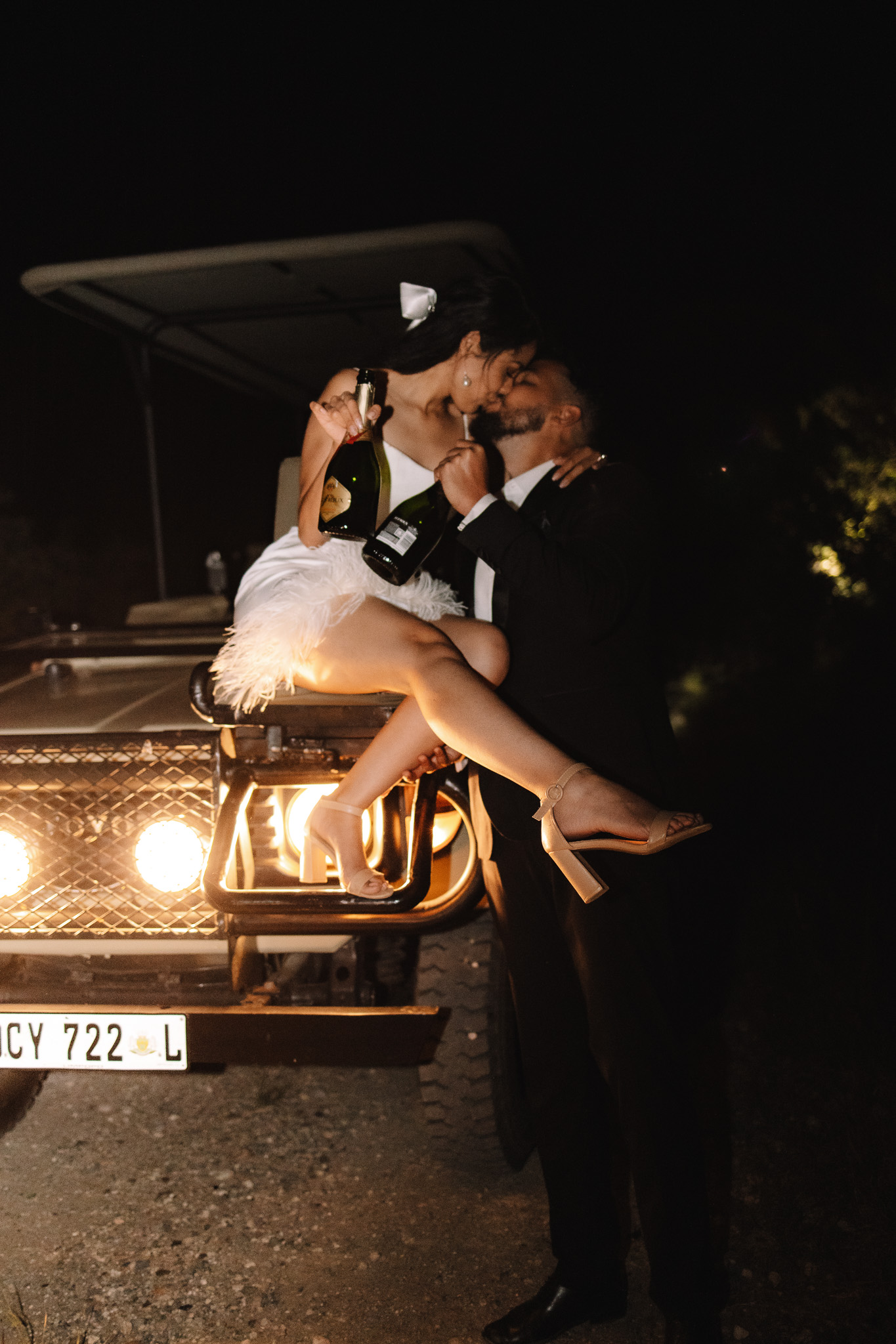 Elopement couple sitting on the front of the safari vehicle kissing and holding a champagne bottle