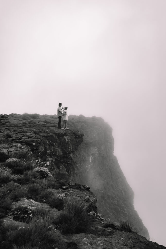 A couple dances on a cliff edge, with mist and greenery from a waterfall in the background at Tugela Falls a South Africa Elopement spot