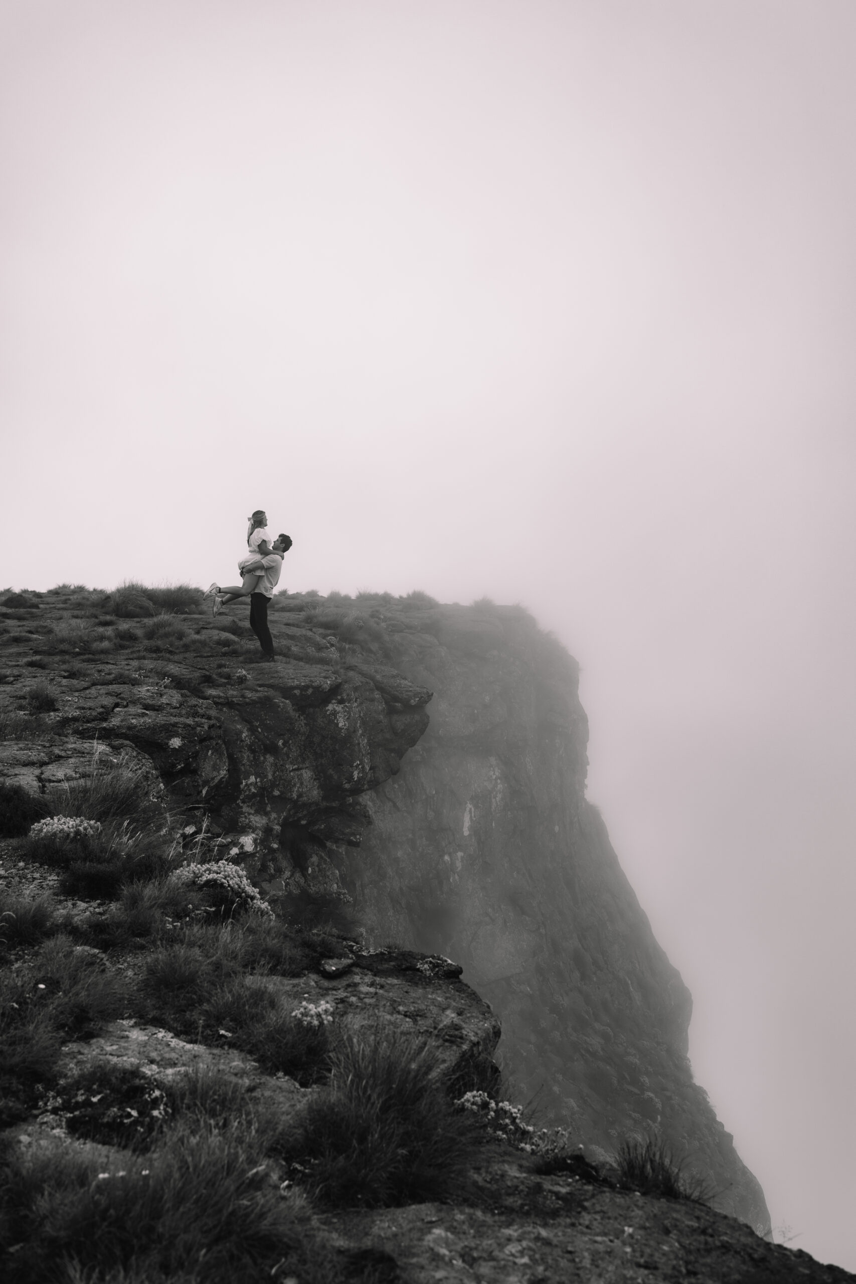 Elopement couple standing on the edge of a cliff at Tugela falls as the mist is rolling up from beneath