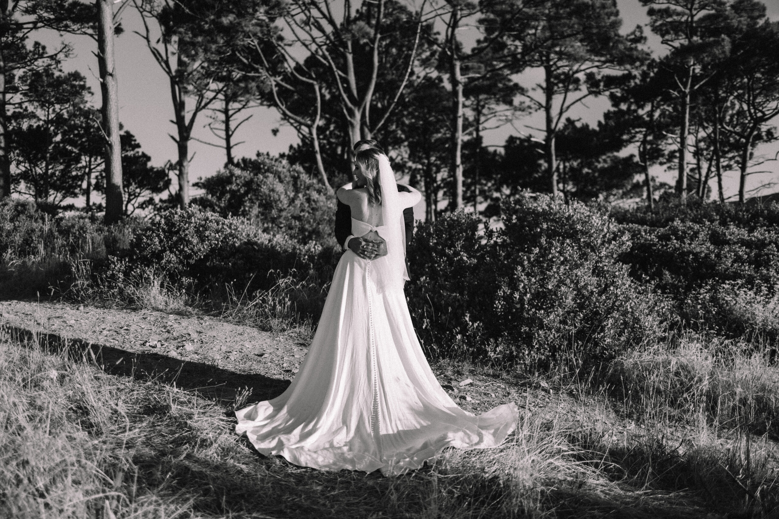 Black and white photo of Bride in a white strapless wedding  and groom hugging in a field