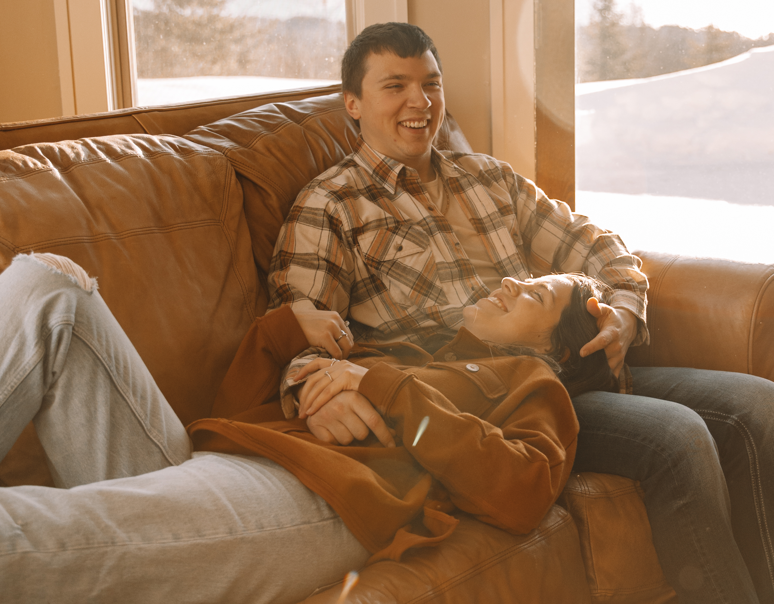 Newly engaged couple sitting together on a couch laughing and relaxing for their engagement shoot in a cozy engagement outfit for their unique engagement photo locations in Minnesota