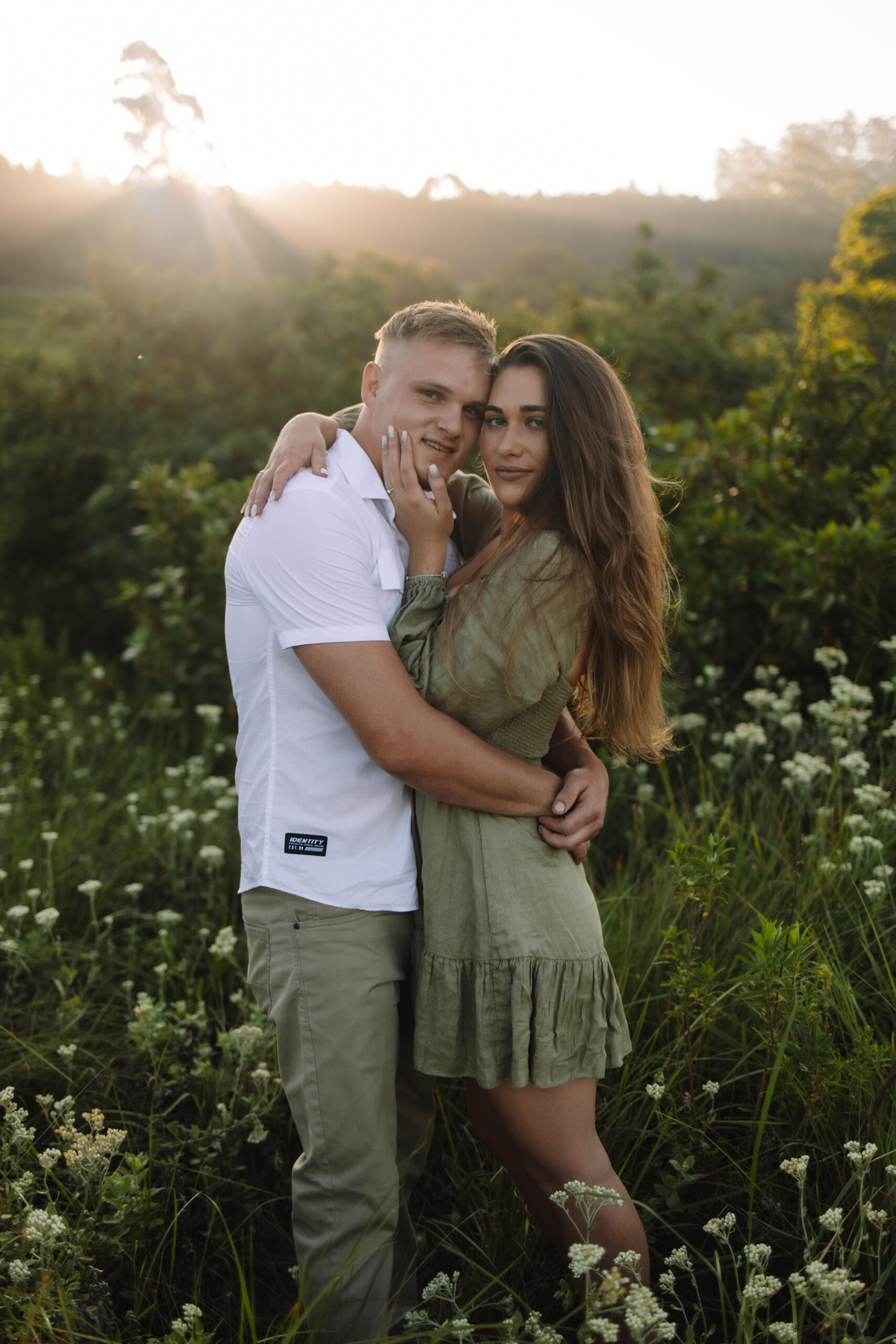 Newly engaged couple hugging in a field of flowers, woman wearing a beautiful green dress and man wearing a white button up and jeans