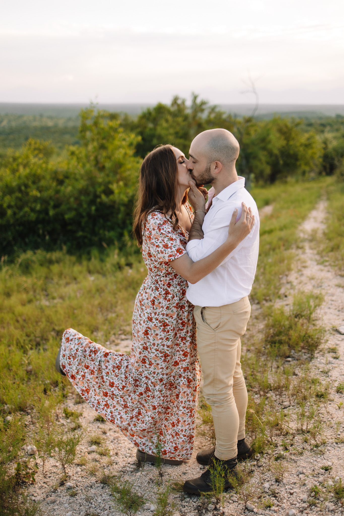 Newly engaged couple kissing in a floral maxi dress and white button up and khaki pants for their engagement outfit