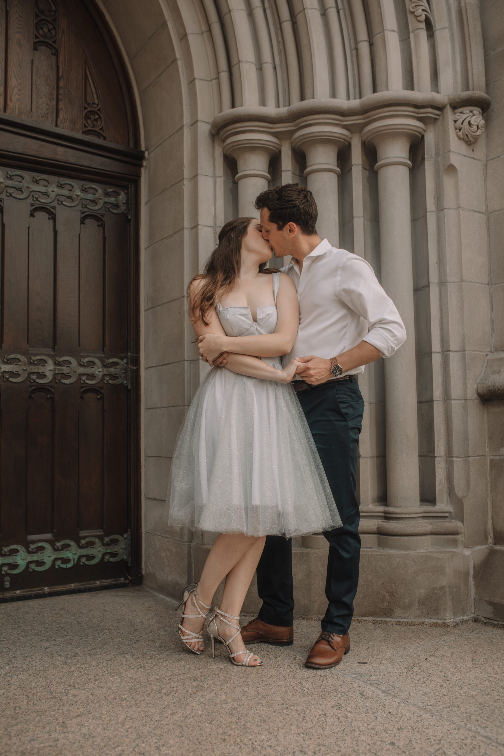 Newly engaged couple kissing in front of a brick building for their engagement photos