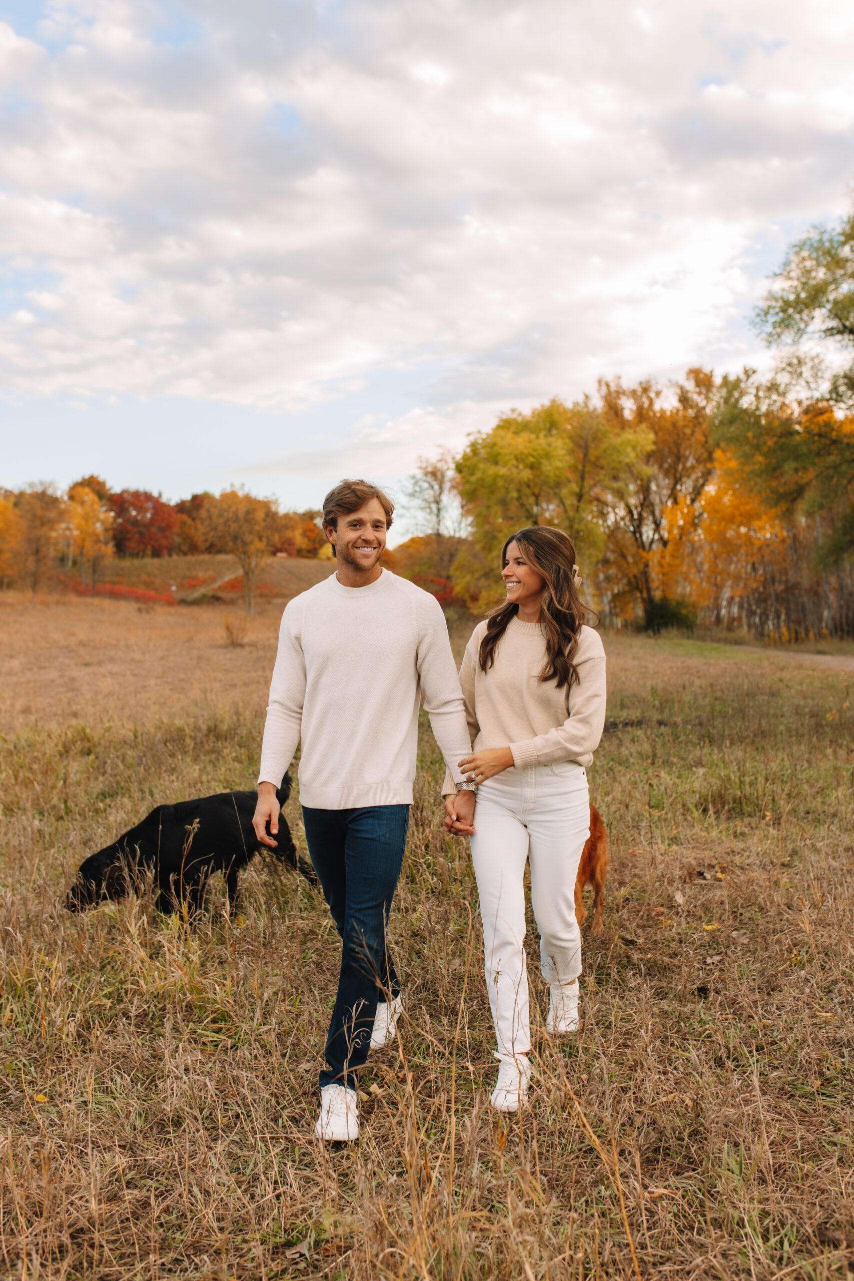 Newly engaged couple walking in a field of grass in fall engagement outfits