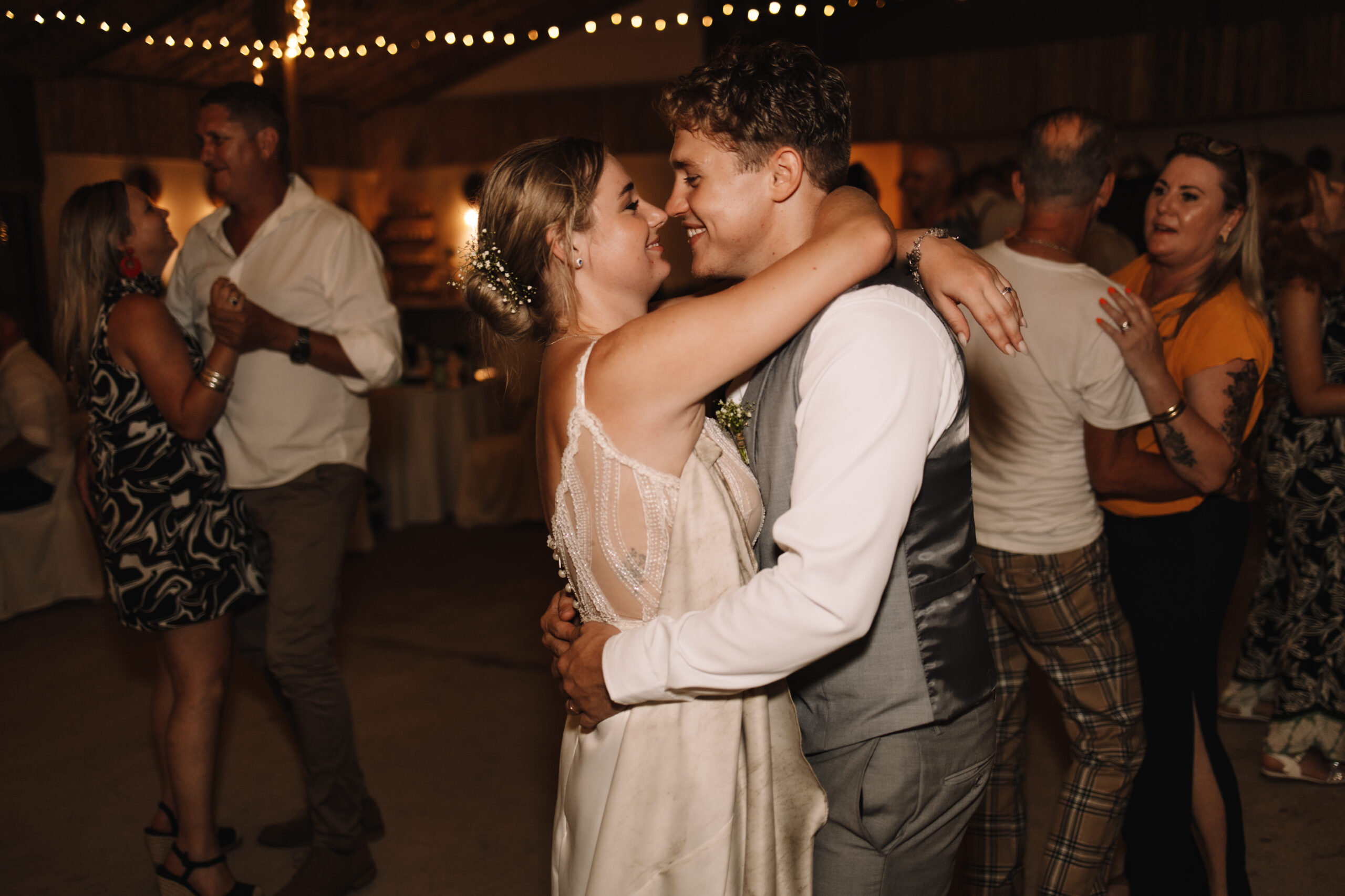 Bride and groom dancing together and holding each other whole touching noses. Guests are dancing and enjoying themselves in the background