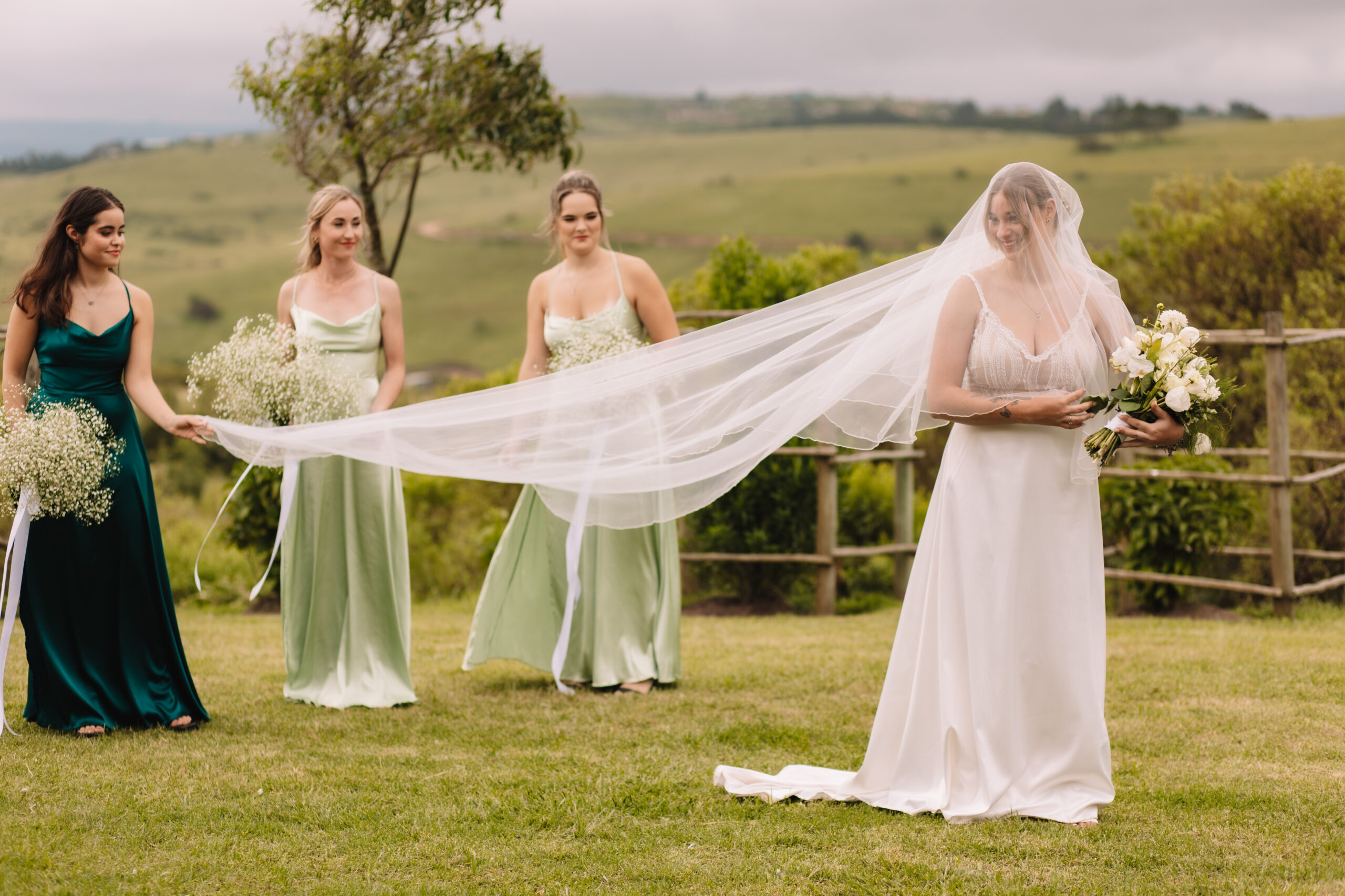 Bridesmaids in green dresses holding bride's veil for 