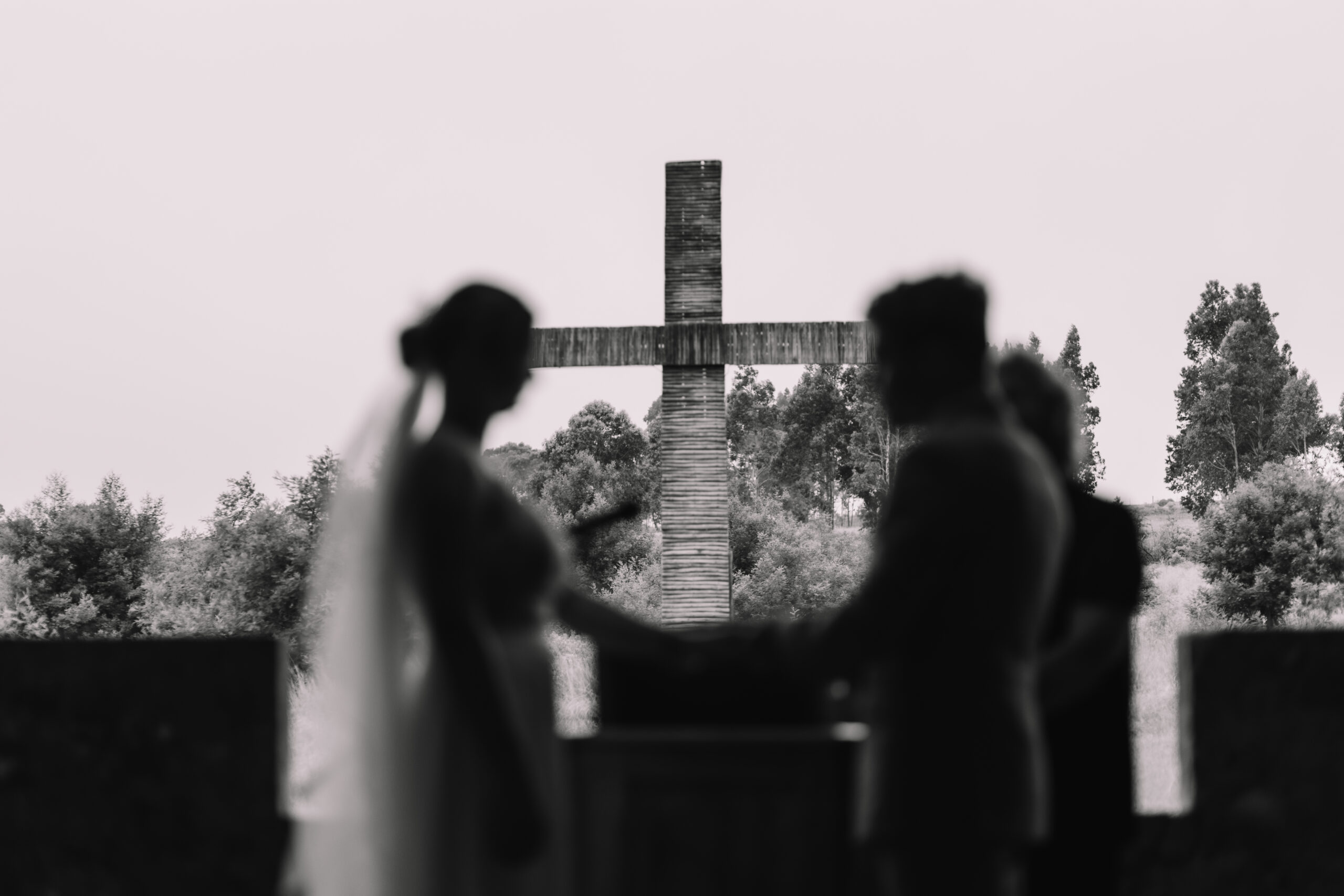 Black and white silhouette photo of bride and groom holding hands in front of the alter with a big cross in the background