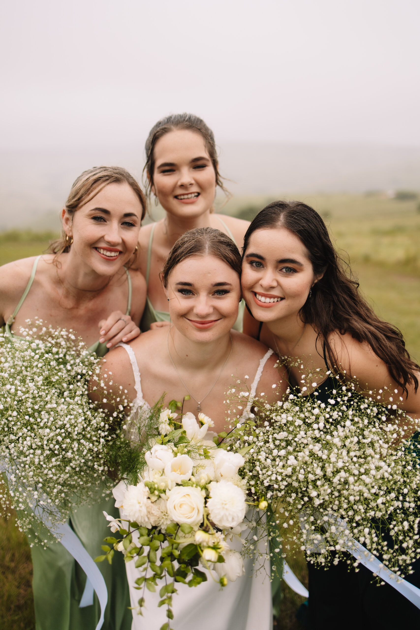 Bride surrounded by her bridesmaids in light green dresses with baby breath bouquets