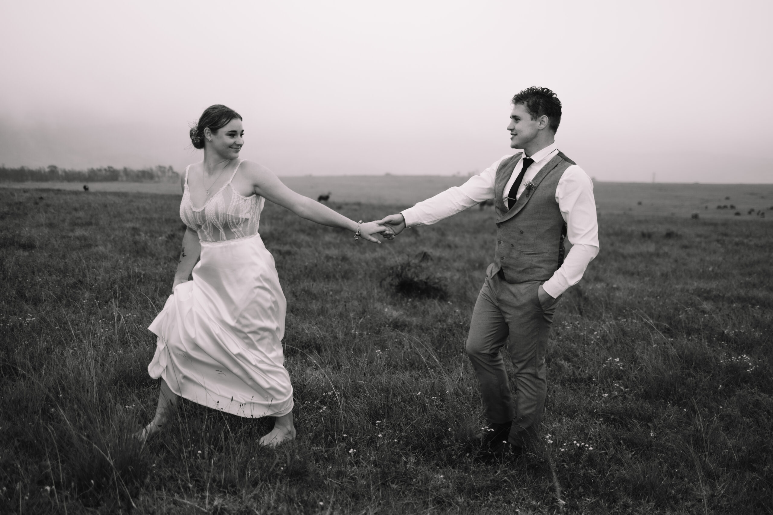 Bride holding her groom's hand while walking and leading him across the field with zebra's walking in the background