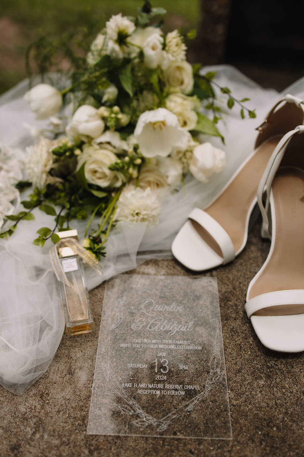 Simple wedding flat lay details with a simple white and greenery bouquet, elegant plain white shoes, a veil and perfume