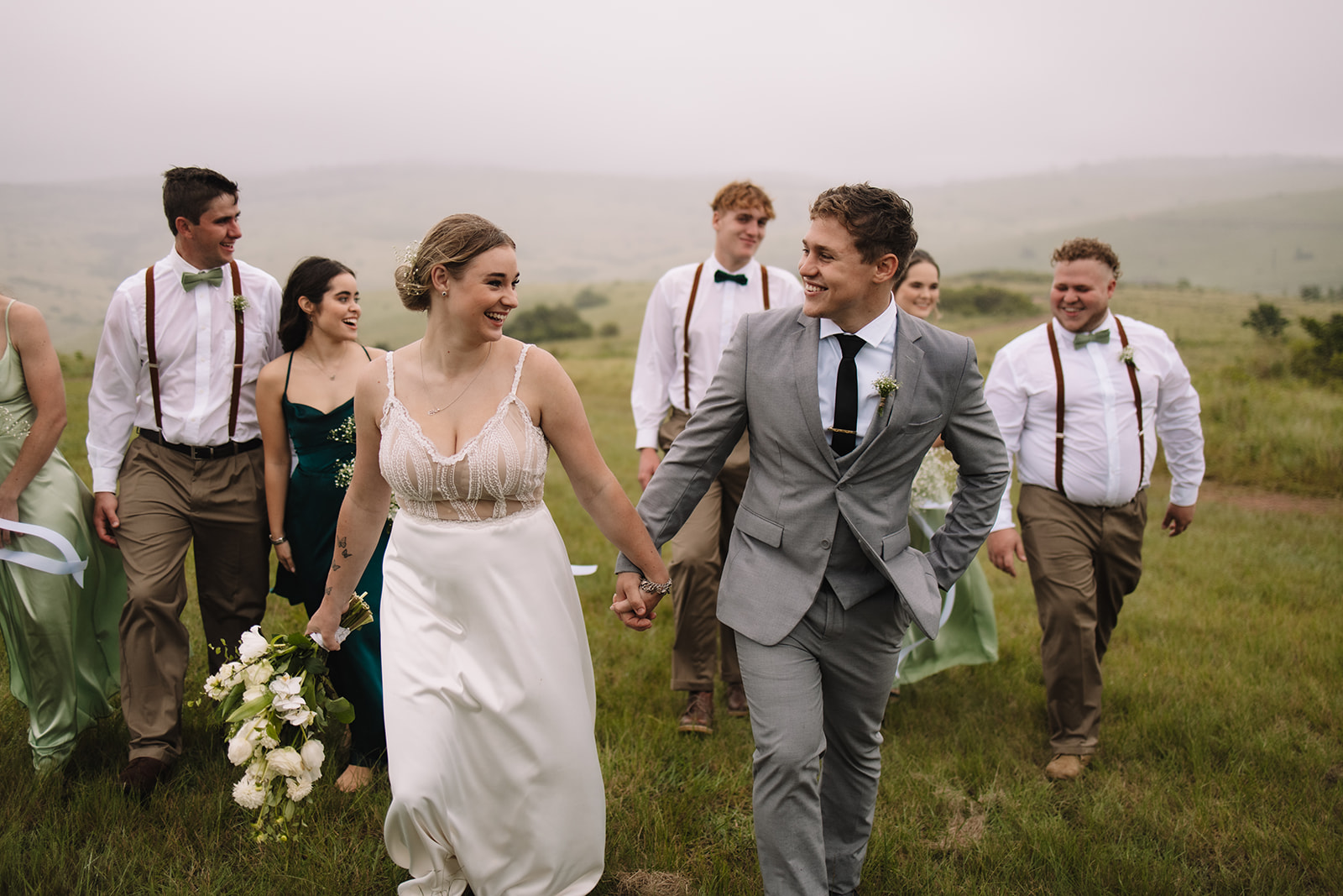 Bride and groom running in a field of grass with their bridal party