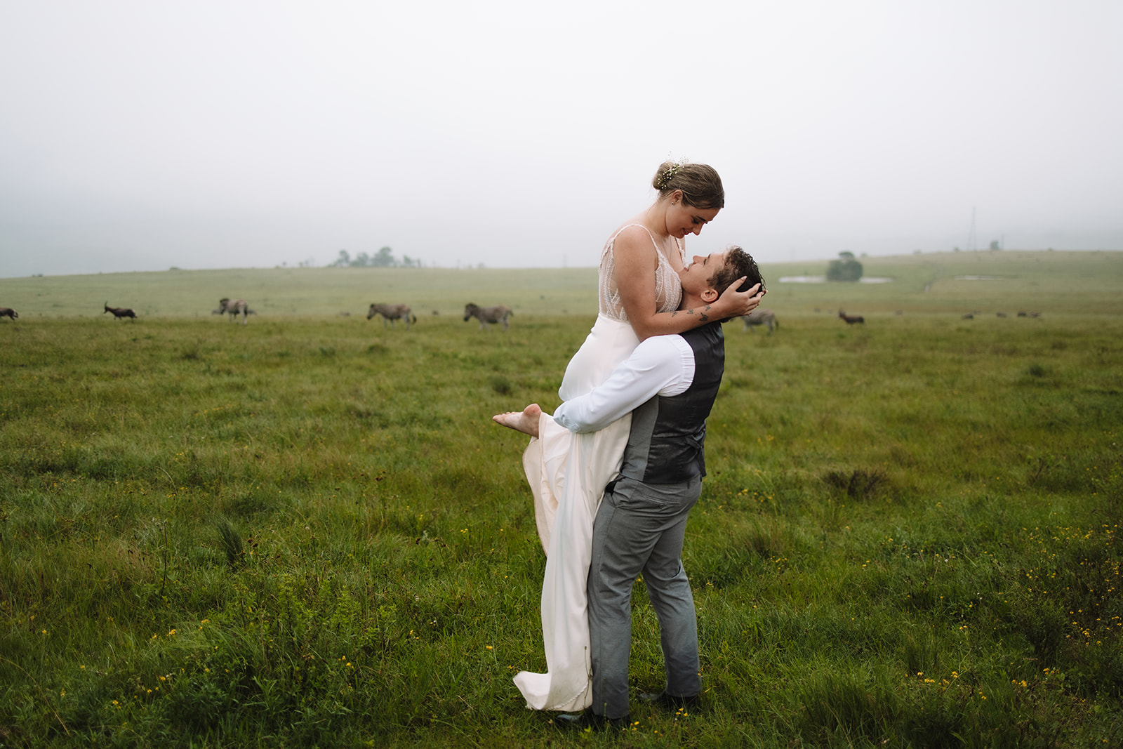 Groom picking up bride in a field of grass in front of Zebra in South Africa