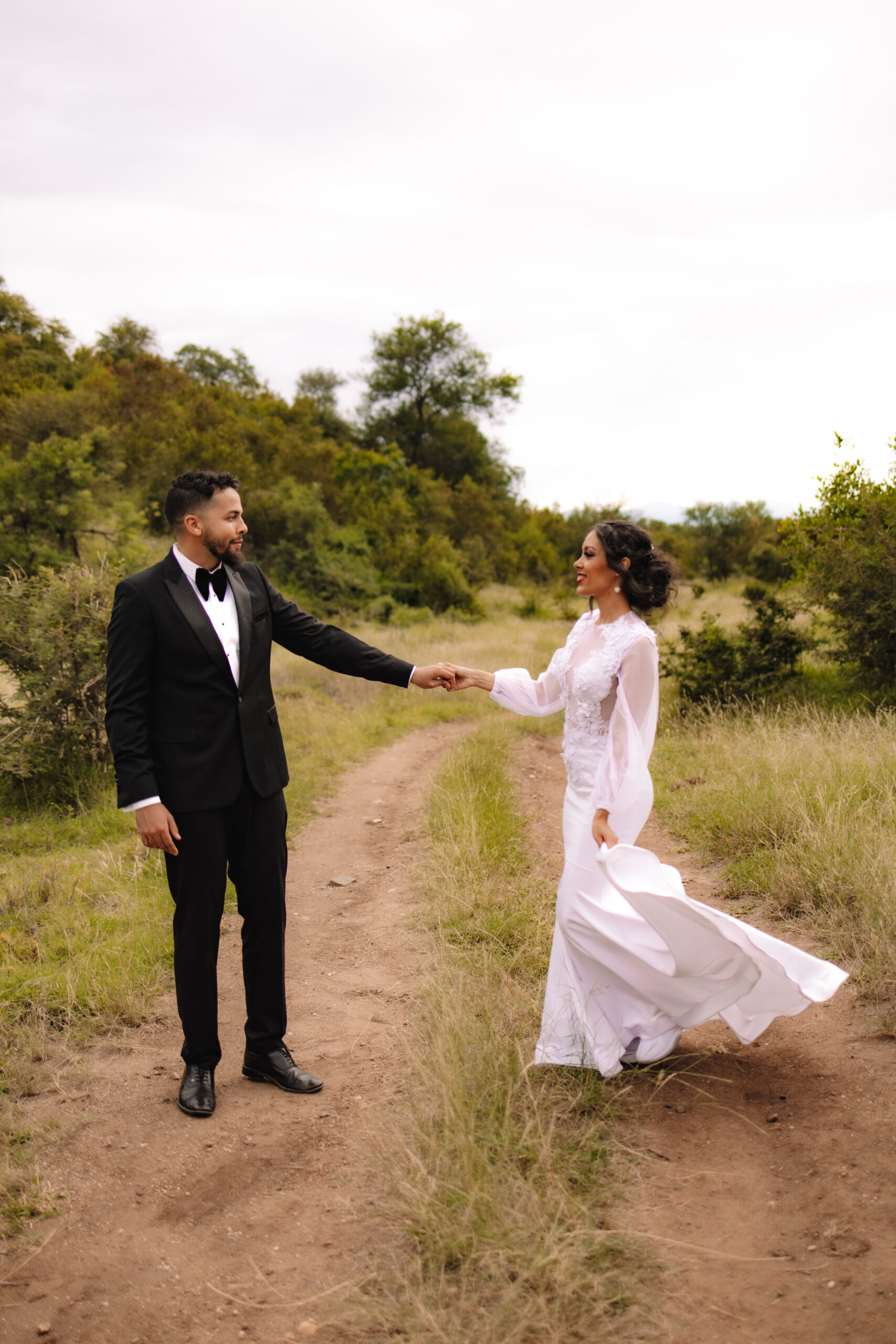 A groom holding his bride's hand twirling her in and out as they stand in a field