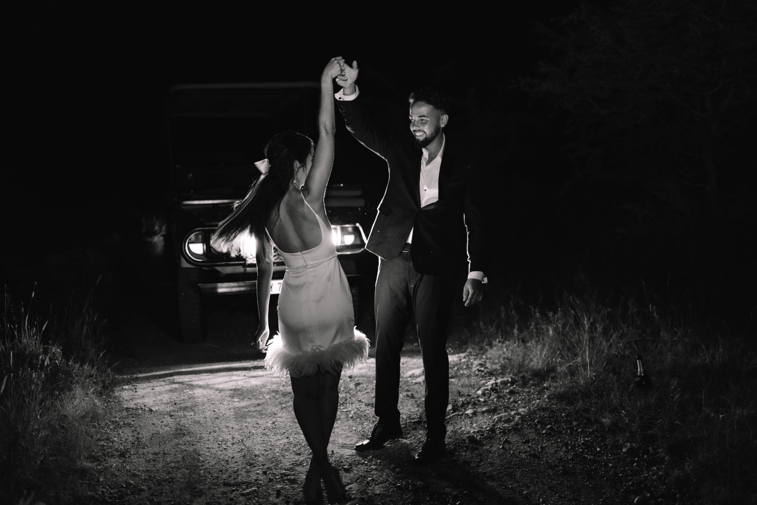 An elopement couple dancing in the dark in front of the headlights of their car