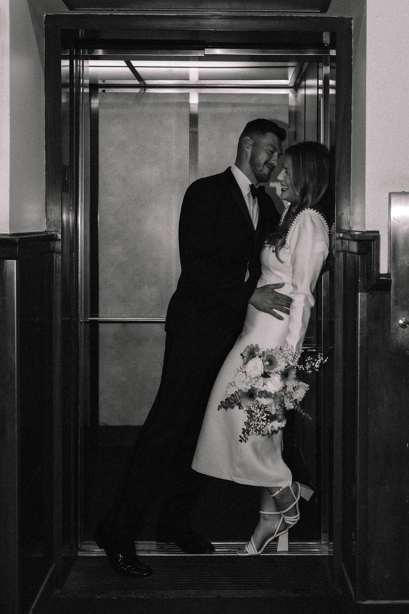 Groom leaning towards his bride as he pushes her against the elevator wall to kiss her