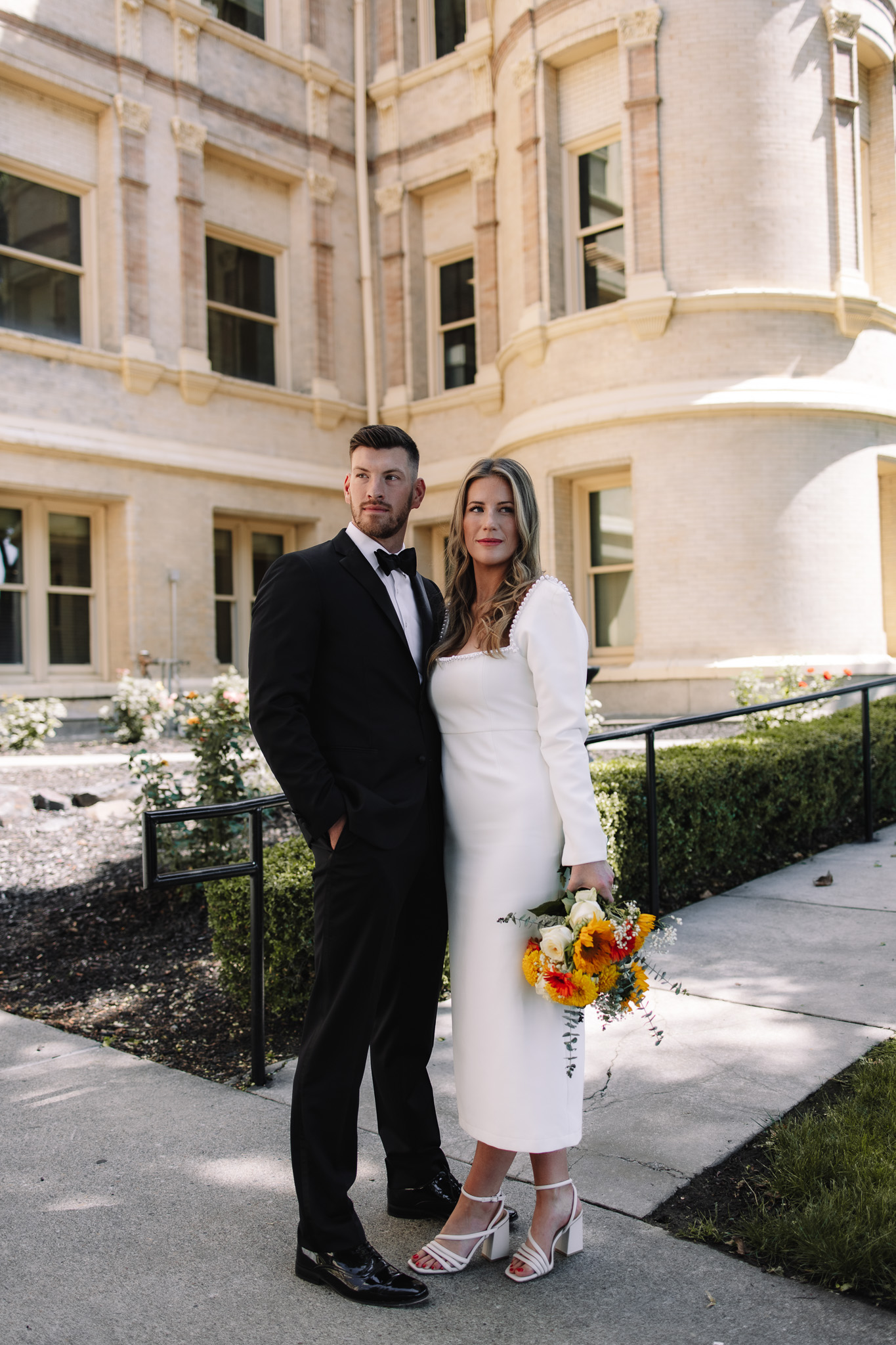 Bride and groom standing side by side in front of the courthouse looking in opposite directions