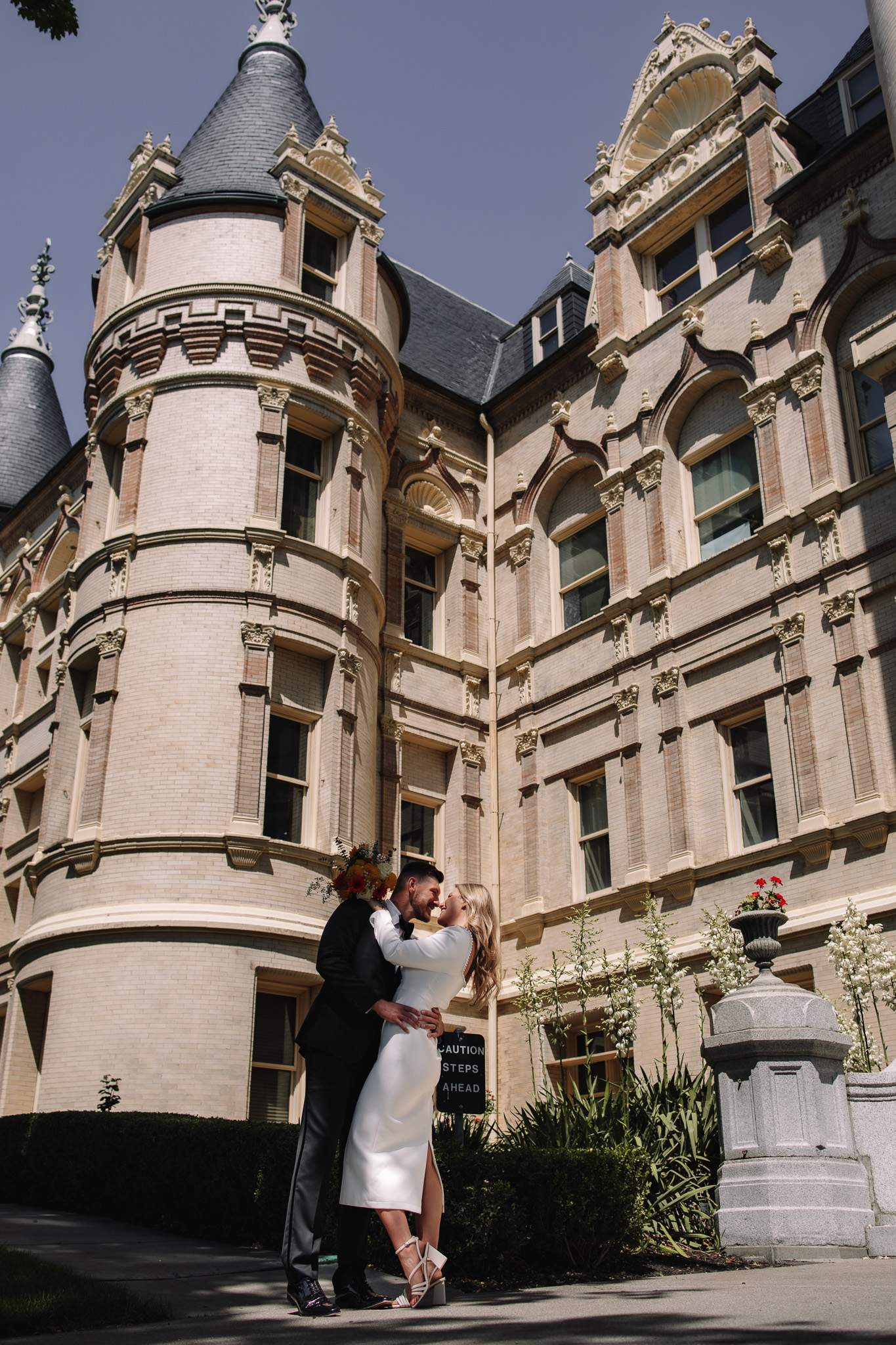 Bride and groom dip kissing in front of a beautiful castle-like courthouse 