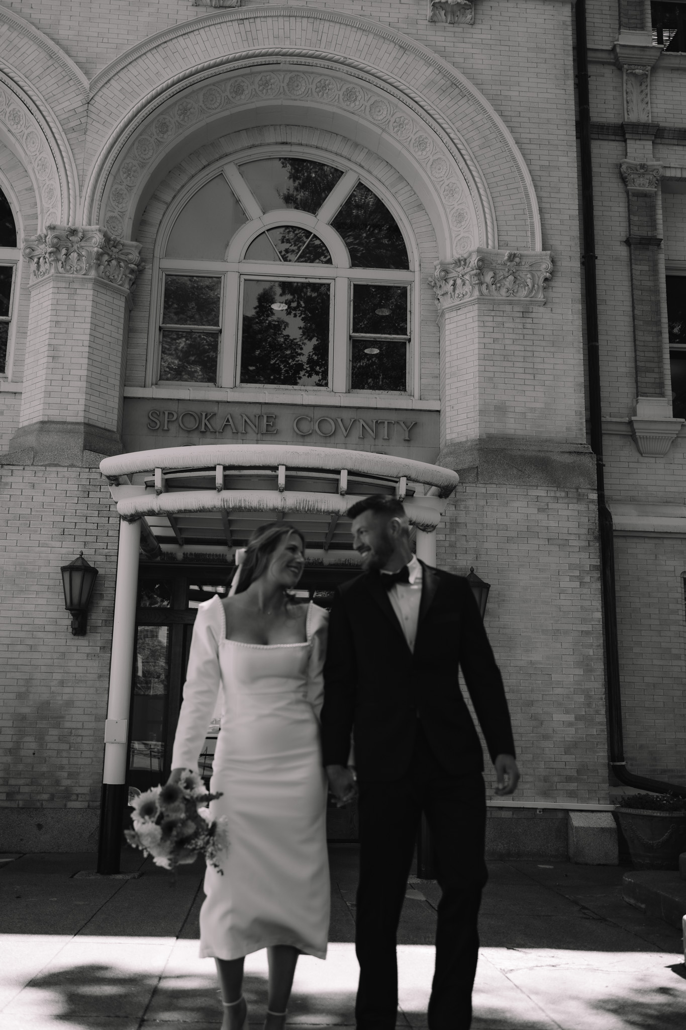 Bride and groom walking happily together bumping hips after getting married at the courthouse