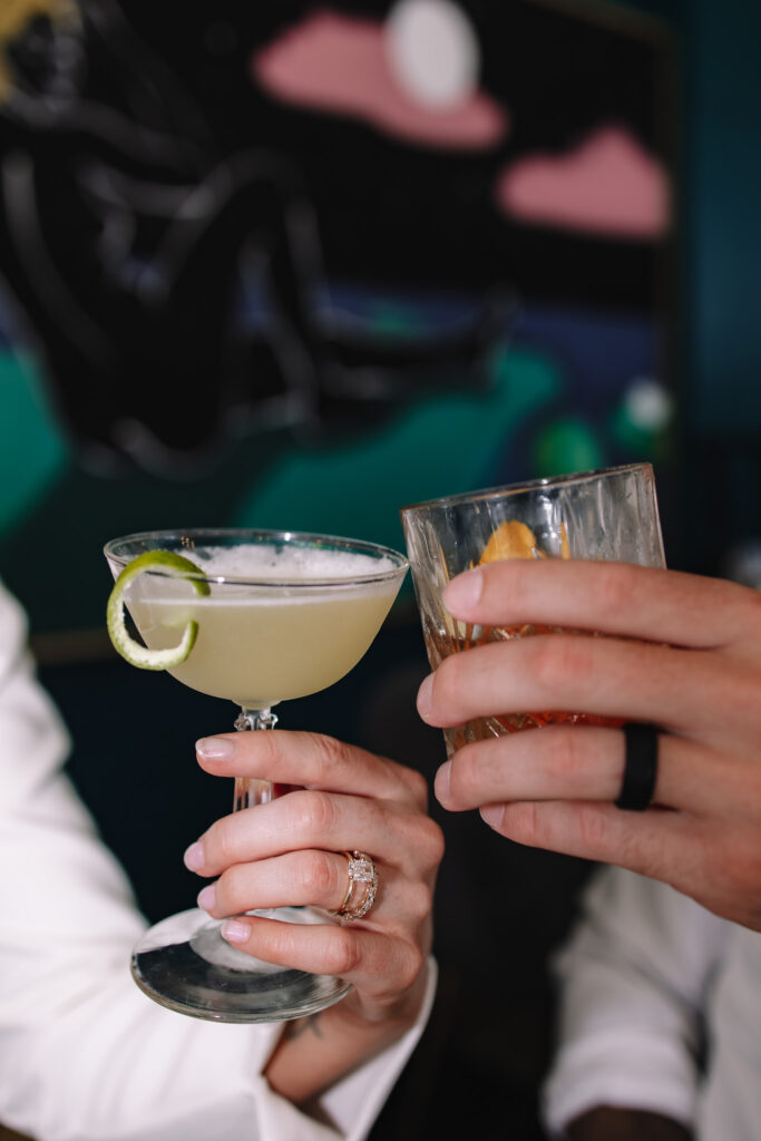 Detail shot of bride and groom clinking their cocktails together with their rings visible