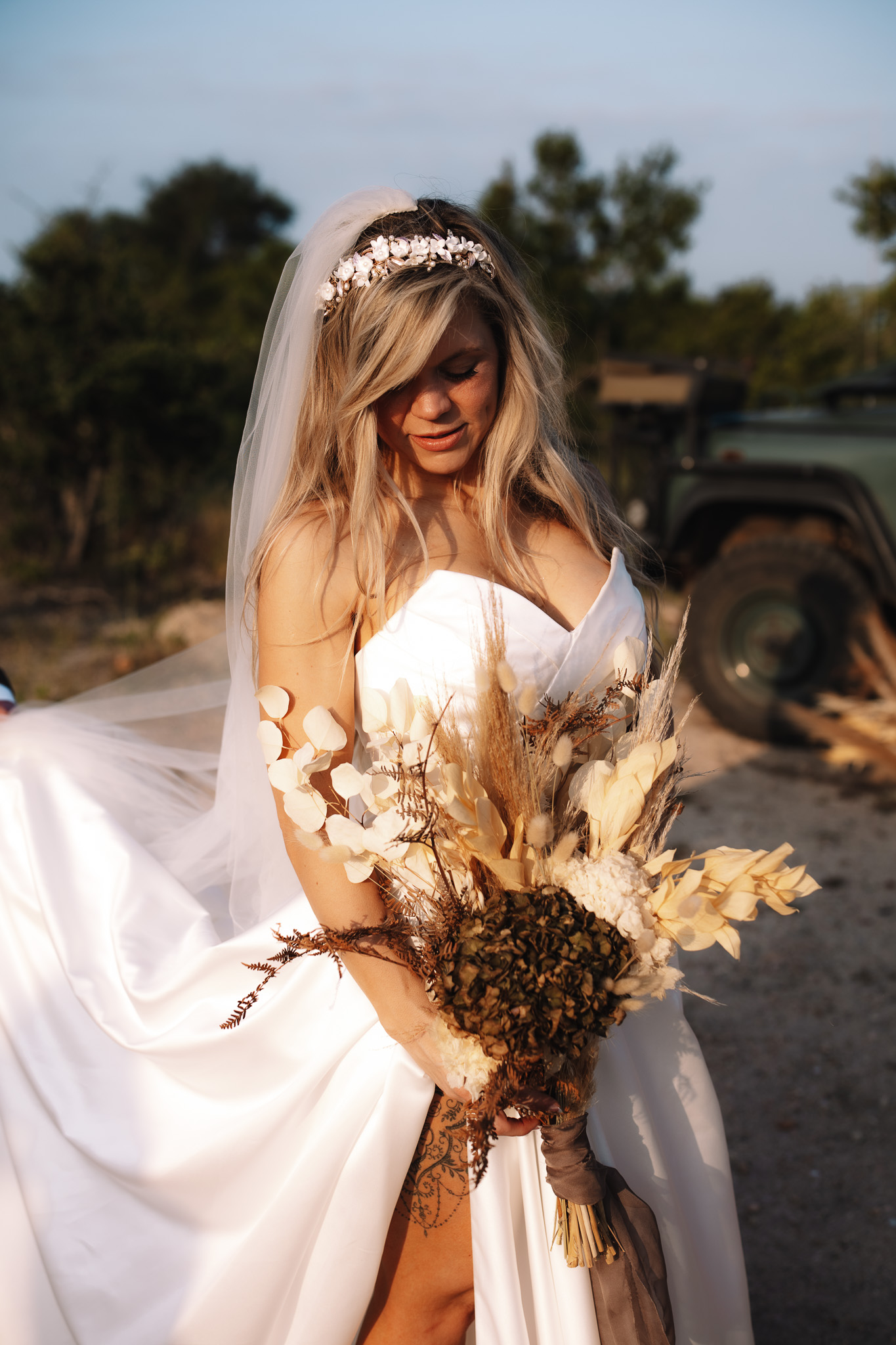 Rustic boho safari bride holding her dried flower bouquet as the sun shines on her dress