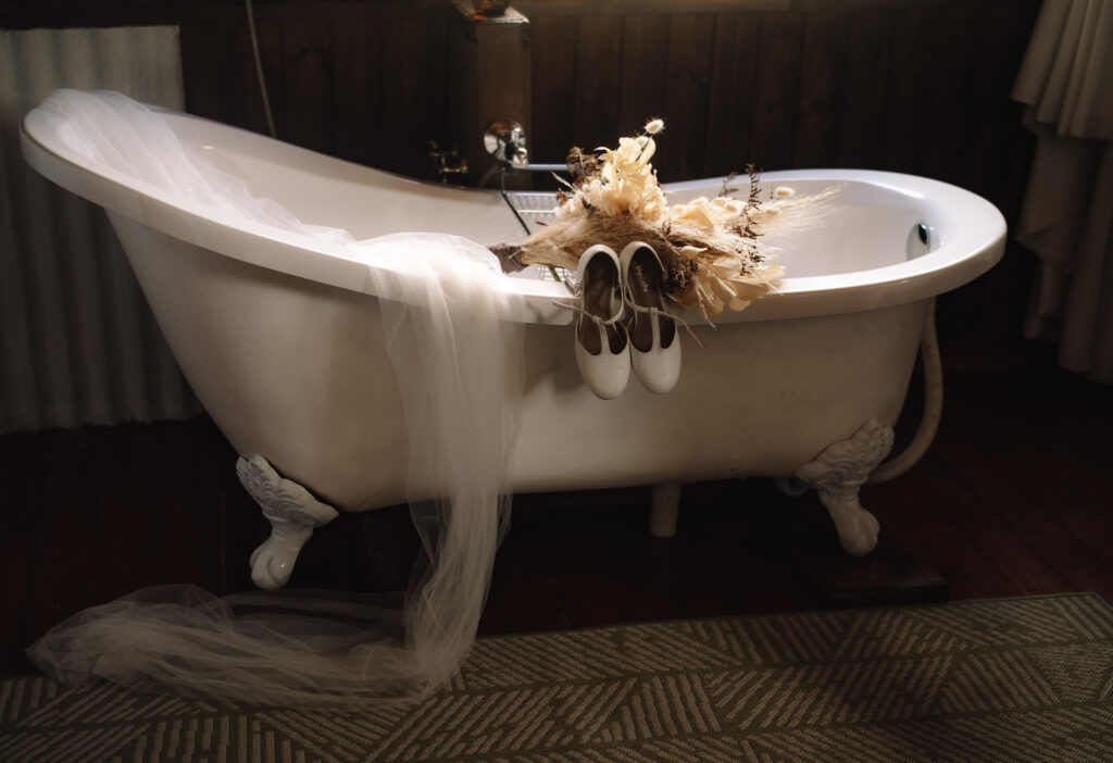 Vintage, rustic safari detail photo of wedding shoes hanging over the bath tub with the veil and bouquet in the shot as well