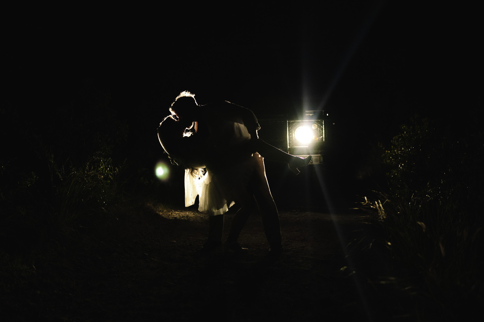 Bride and Groom silhouette shot of groom dip kissing his bride in front of the safari vehicle's headlights to end off their special intimate safari wedding in South Africa